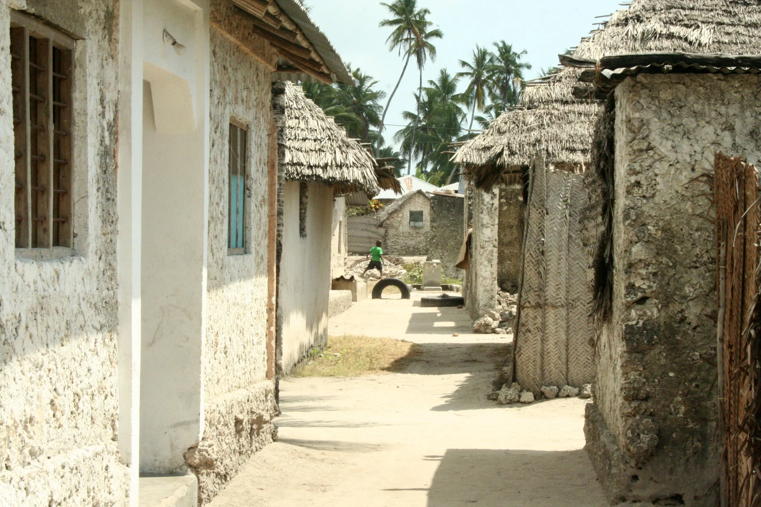 A narrow sand passage between coral-stone houses in the village the crew calls home, with its thatched roofs, dust and hand-built walls, in a contrast to the open water beyond.