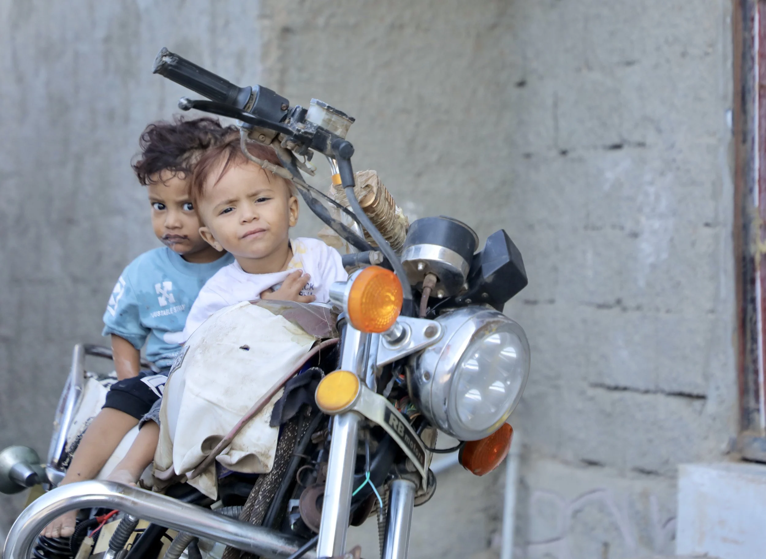 Sami’s nephew, and young son  Azan sit on a motorbike outside the house while adults gather nearby.