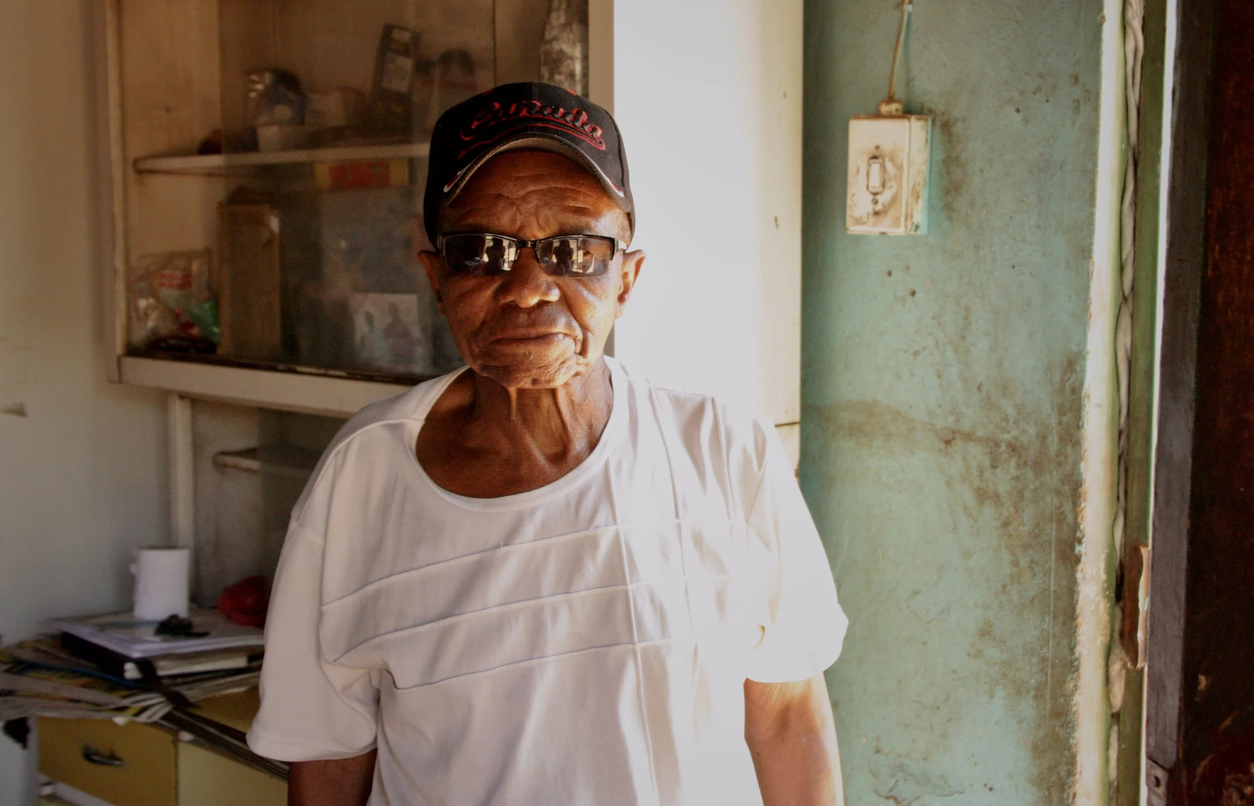 Michael Mosabala Leschibi, 78, stands inside his home in Ha Chonapase, Leribe District. He raises his two grandchildren on an old-age pension after taking them in when their mother repeatedly disappeared and left them without care.