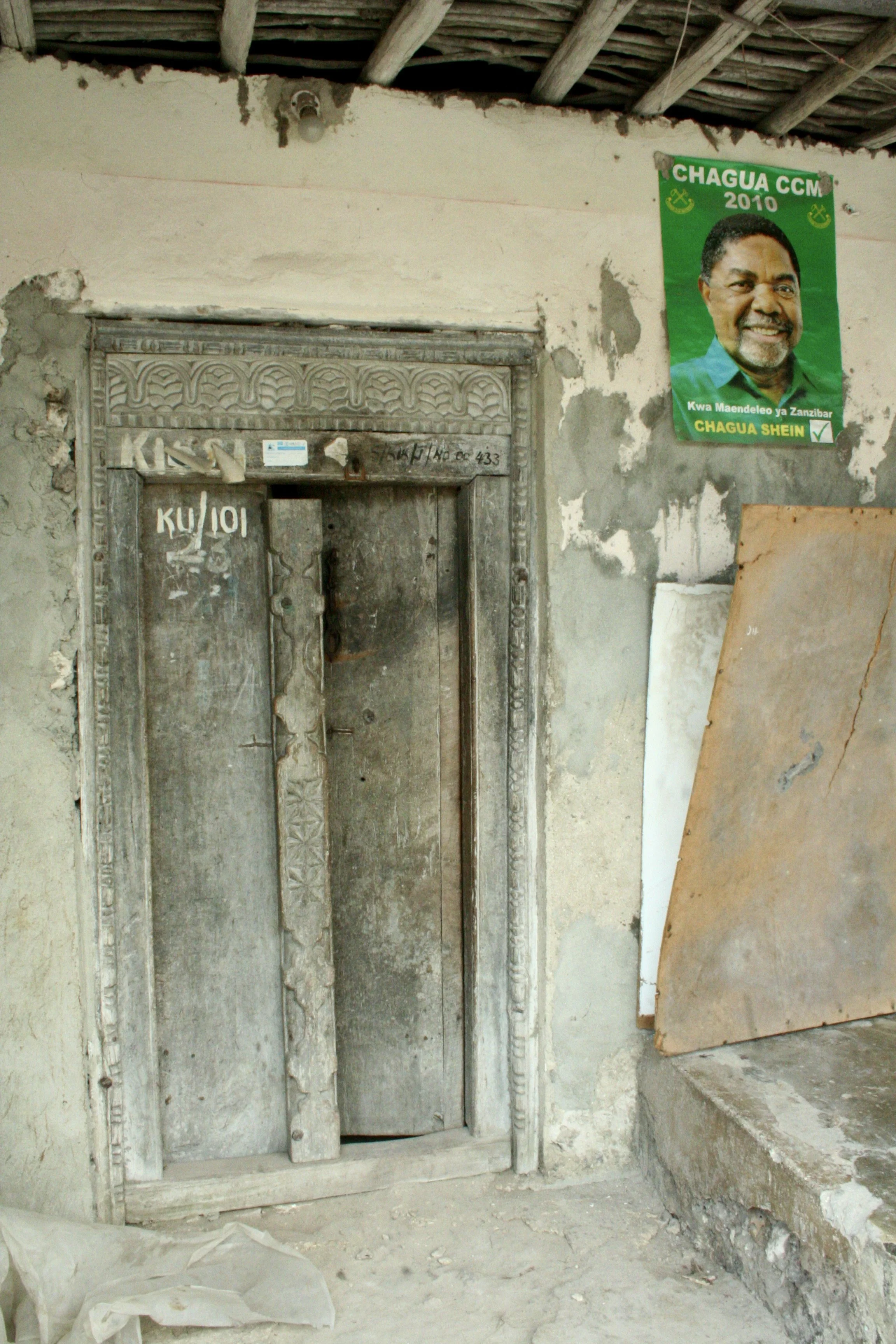 A traditional carved Zanzibari door, its craftsmanship as old as the fishing techniques practised nearby. A campaign poster for October 2011's Igunga by-election is pinned above it as an incidental record of the political moment the series was shot i