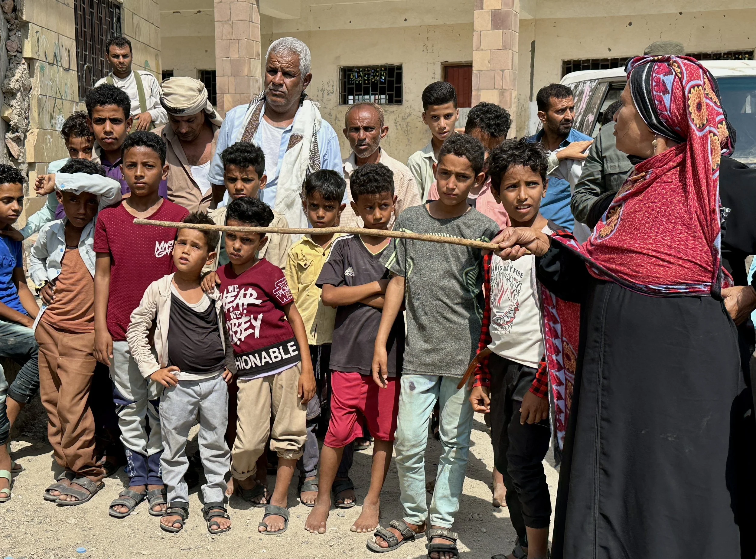 A local woman speaks to residents during an Explosive Ordnance Risk Education session in Taiz, Yemen, as children and community members listen nearby. Awareness campaigns encourage civilians to report suspicious objects and avoid touching unfamiliar 