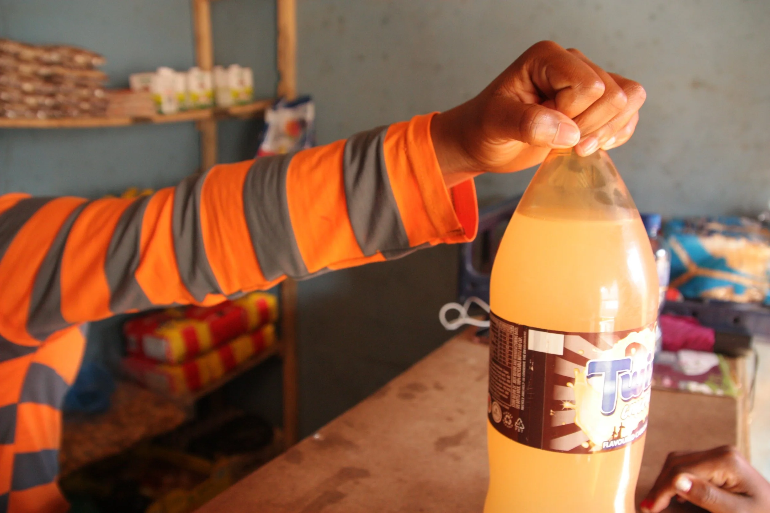 A customer purchases a soft drink inside Paballo’s shop. Small neighbourhood stores like this one often become informal social spaces as well as sources of income within the community.