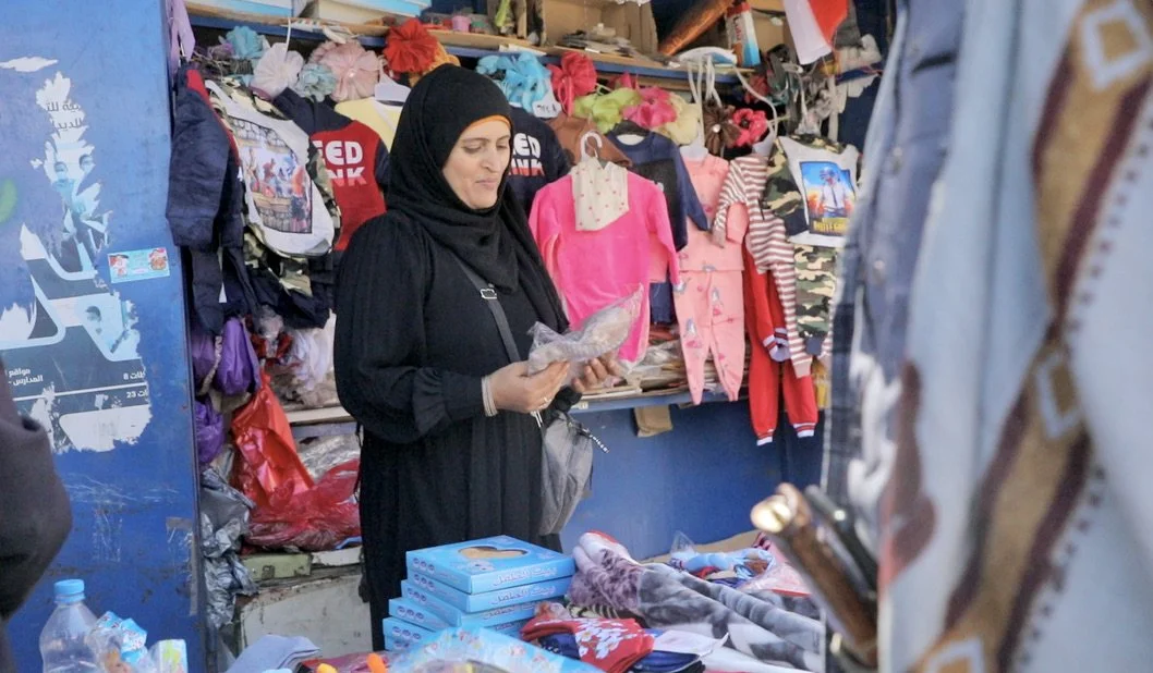 Dalila Abdo Ahmed stands at her clothing stall in Taiz, Yemen. After losing both legs in a landmine explosion on her wedding day in 2018, Dalila gradually rebuilt her life and now earns her own income through the small business, using the money to su