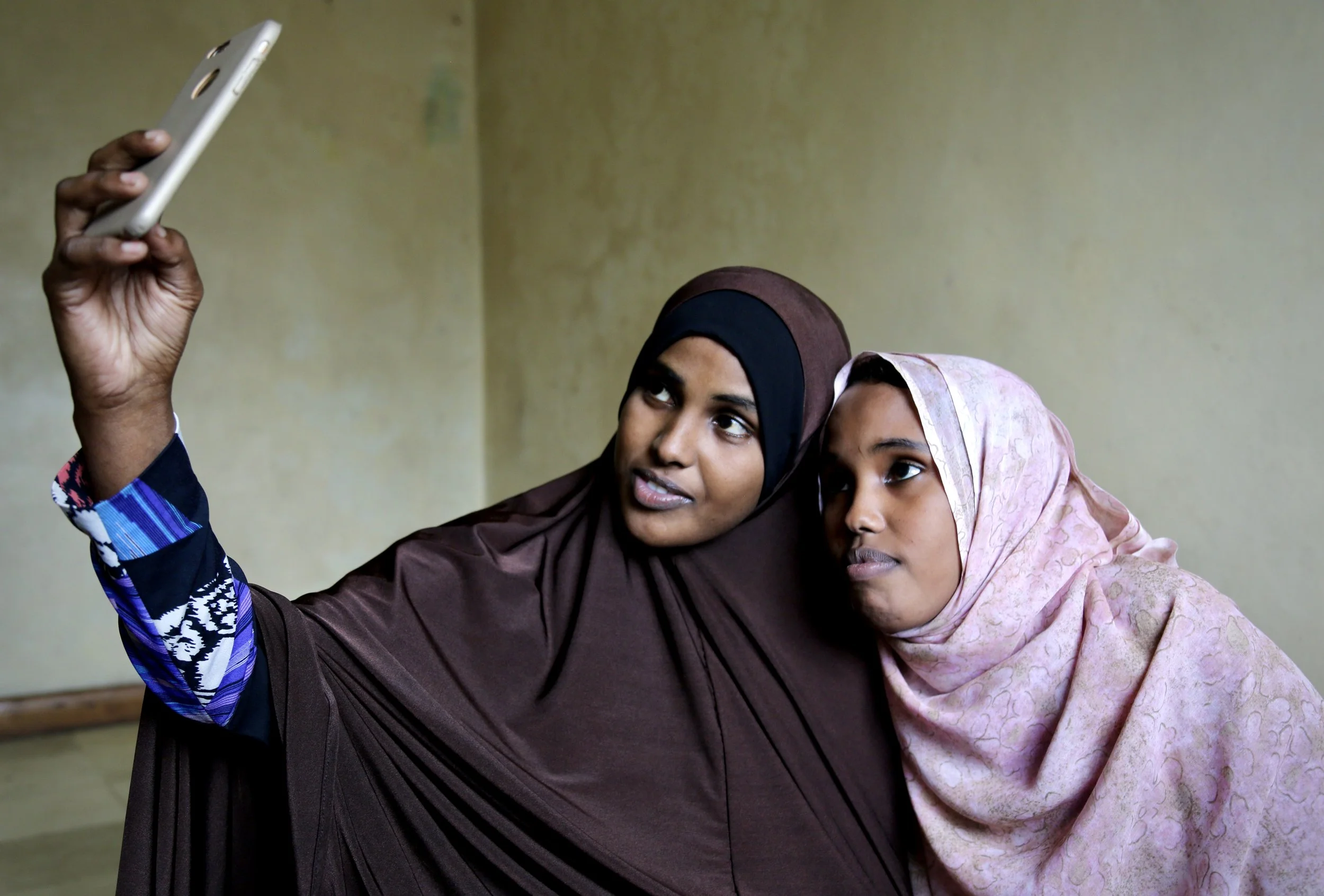 Two Somali refugee sisters look at a mobile phone inside their apartment in Eastleigh, Nairobi. The women remained in contact with relatives and friends who were still living in Kakuma refugee camp. Nairobi, Kenya, June 2016.