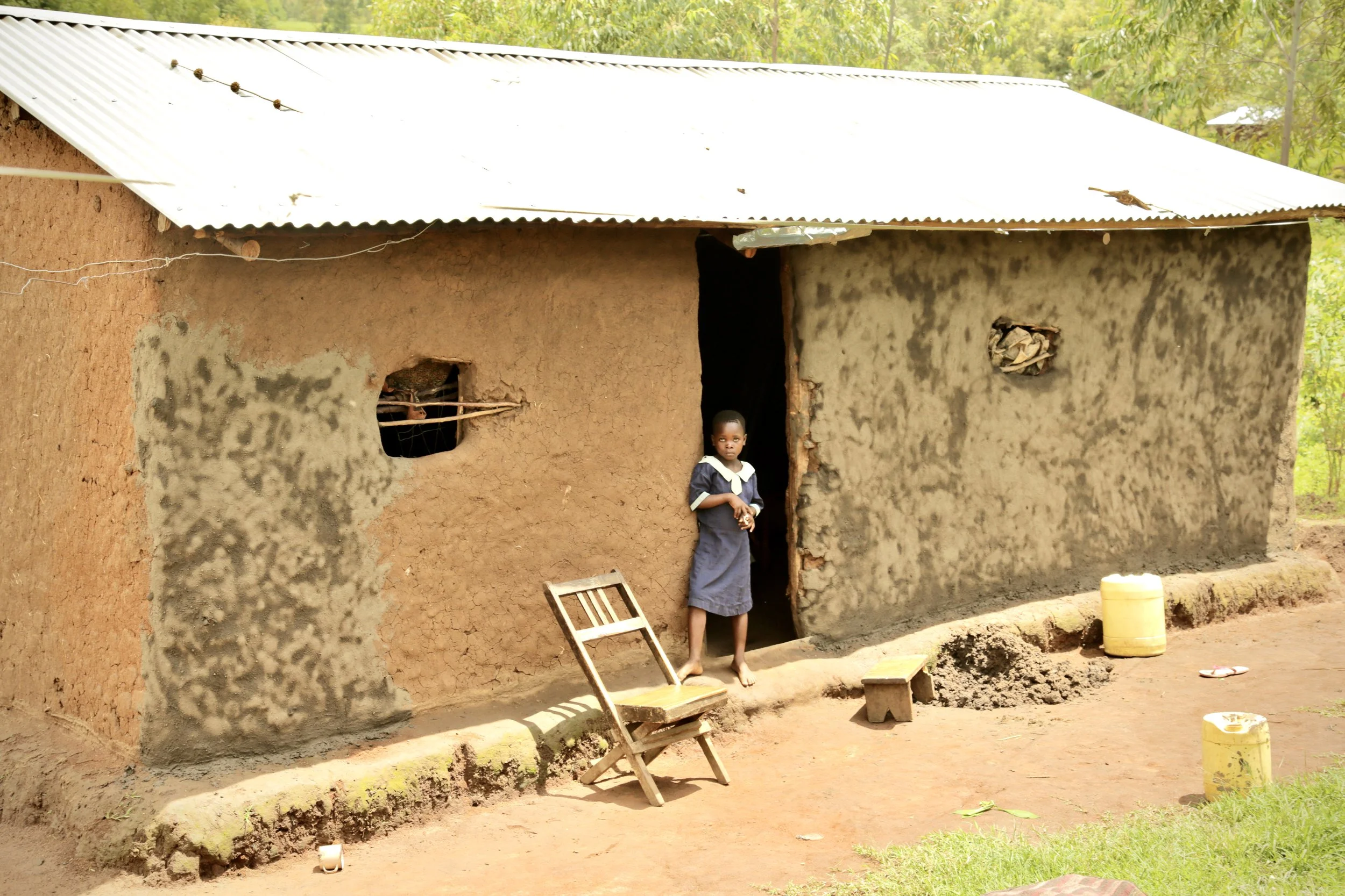 A pupil at Albertos Divine Providence School stands outside her family's home in Kakamega County, Kenya. Children in the community often balance schoolwork with household responsibilities, including helping to collect and store water for daily use.