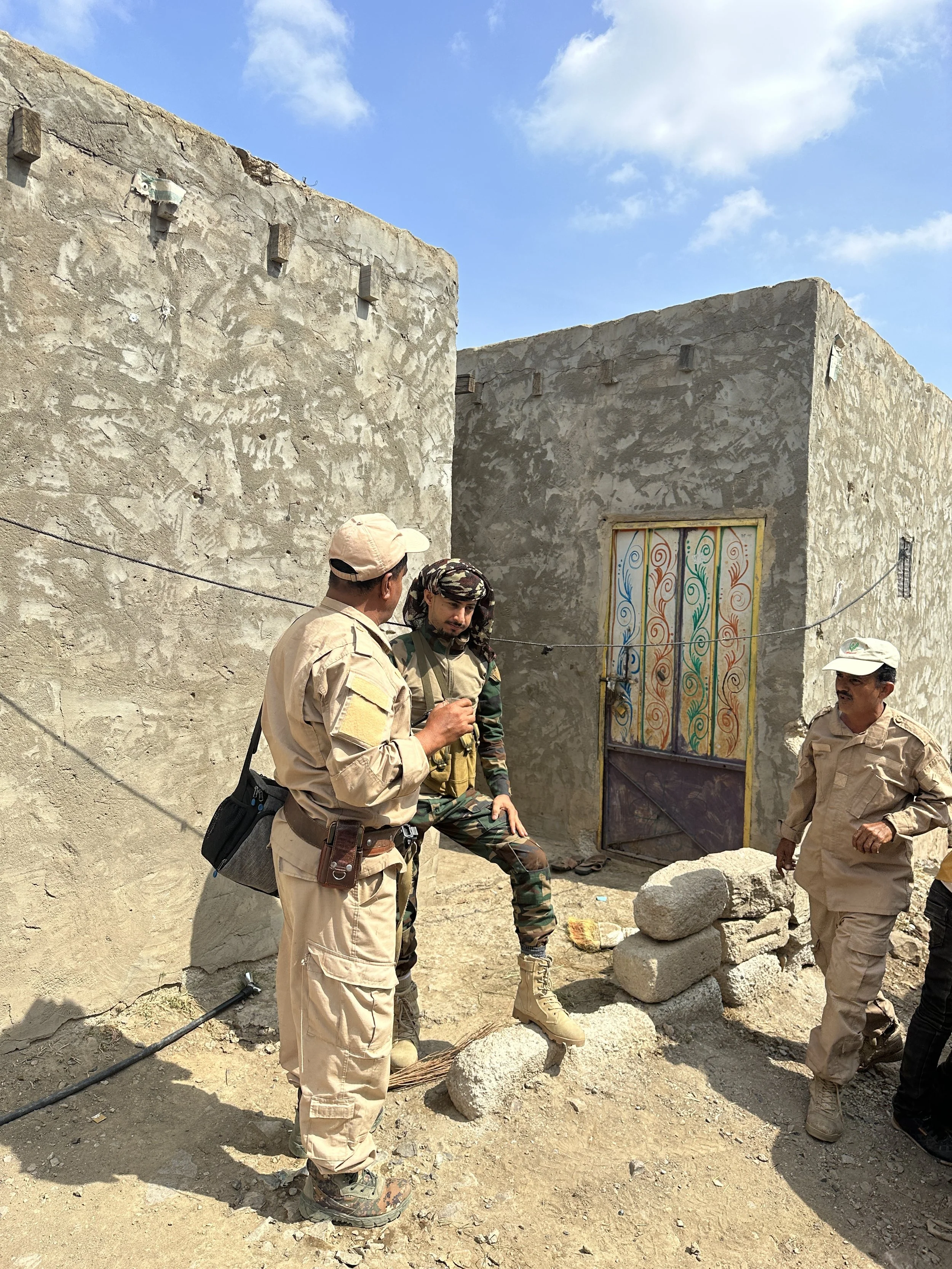 Project Masam demining team members in discussion with a local security escort outside a home in Al Dhale Governorate. The demining teams work in close coordination with local security to operate safely in areas where Houthi forces planted landmines 