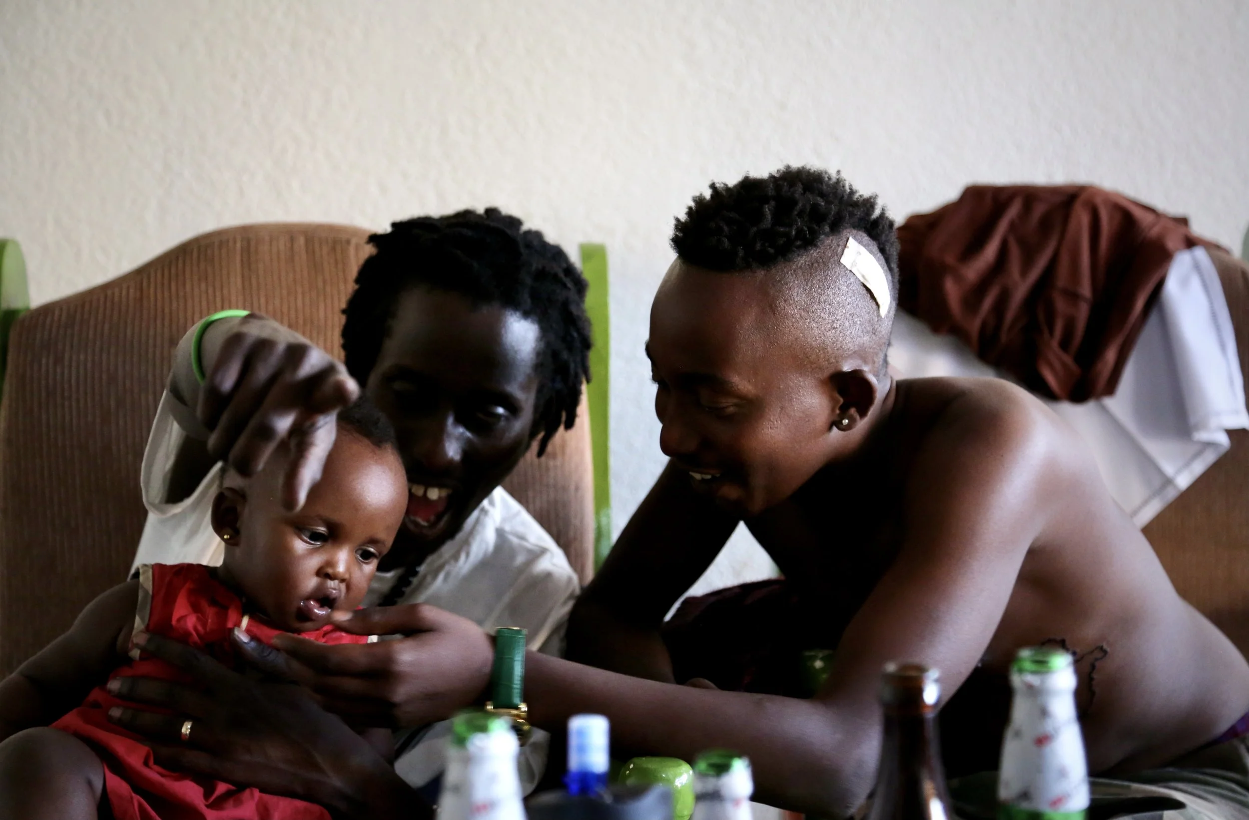 Two young Burundian refugees, father Bertrand  Ninteretse and godfather Venuste Maronko play with nine-month old Shikiro inside the Kigali house where several exiled activists and former protesters lived together after fleeing Burundi in 2015.