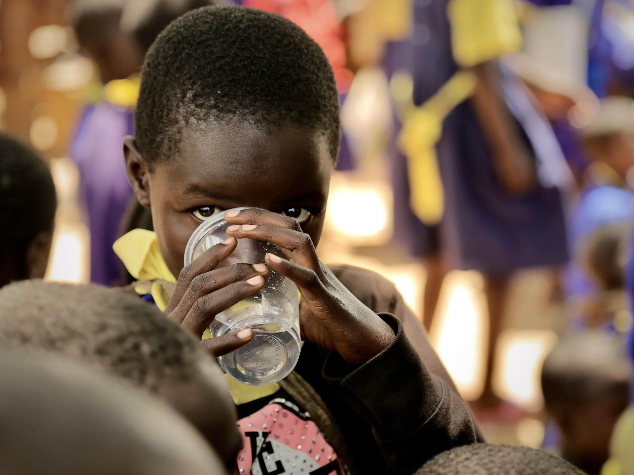 A pupil drinks water during a school gathering at Shinyunzu Primary School. Access to safe drinking water allows children to focus on ordinary parts of school life rather than the challenge of finding water.