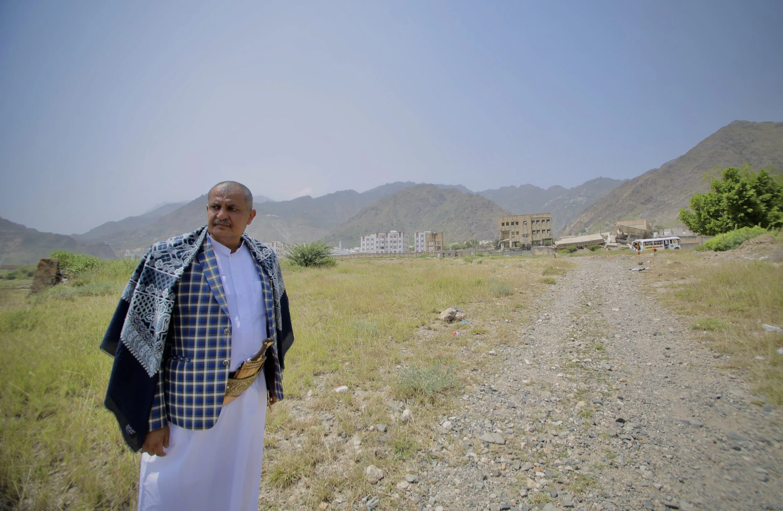 The local Director of Education (Taiz Governorate) stands near contaminated land on the outskirts of Taiz, Yemen. Former frontlines around the city remain heavily affected by landmines and unexploded ordnance, restricting movement and threatening nea