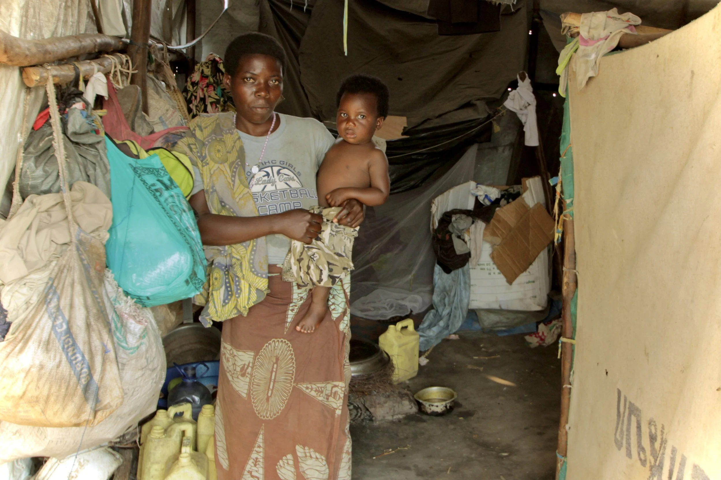 A woman holds a child outside her shelter in the camp, where many families displaced by violence around Bujumbura were living with limited assistance.