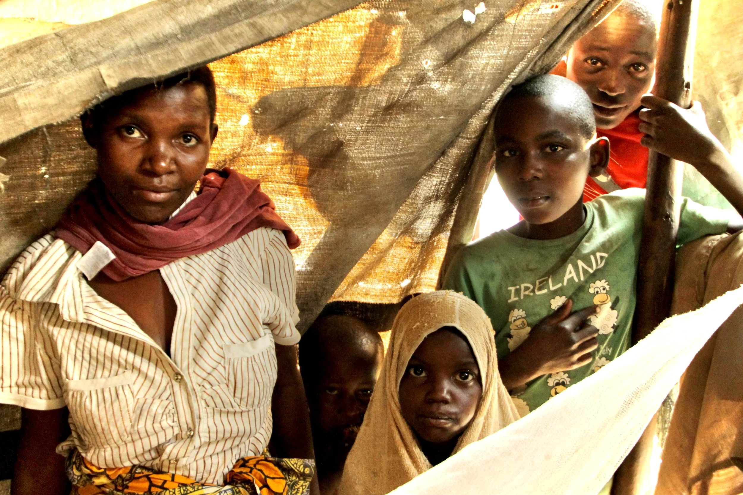 A woman stands with childrenn inside a makeshift shelter, illustrating the difficult conditions in which many displaced families were living.