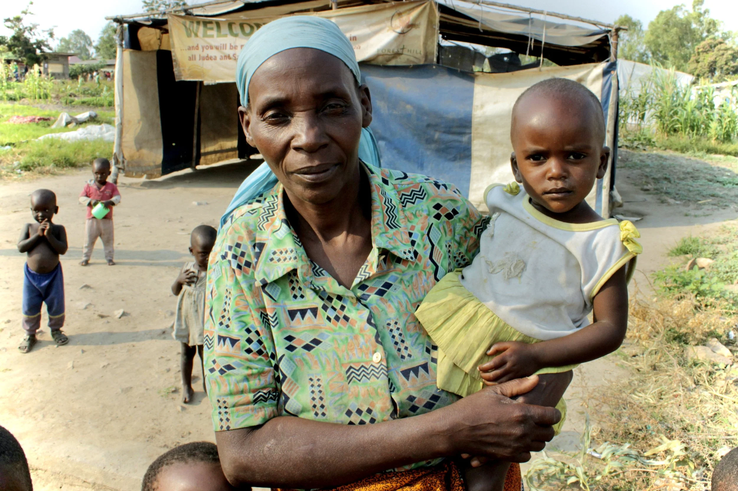 An older woman carries a child outside her shelter in the displaced persons camp, where several generations of families uprooted by Burundi’s 2015 crisis were often living together in fragile conditions.