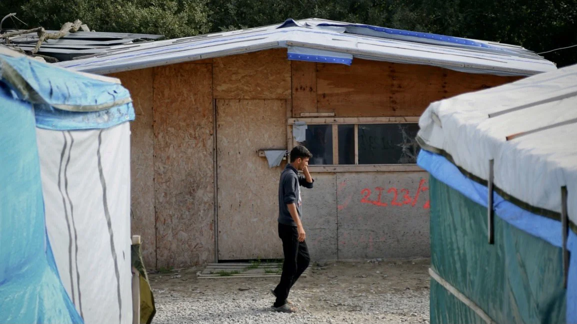 A lone child walks between shelters in the Calais “Jungle” camp shortly before French authorities moved forward with demolition plans. Aid workers feared hundreds of unaccompanied minors would disappear into homelessness, trafficking networks, or fur