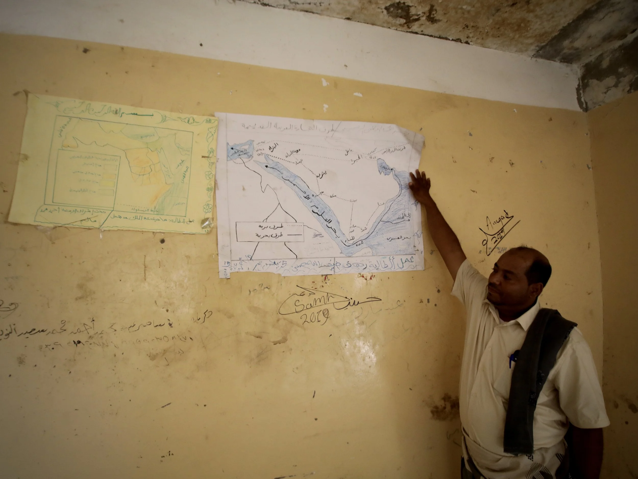 School Director Ahmad Mohamad Al Barakani points to hand drawn educational maps of Yemen still hanging inside a damaged classroom at Al Shaab School in Taiz governorate.