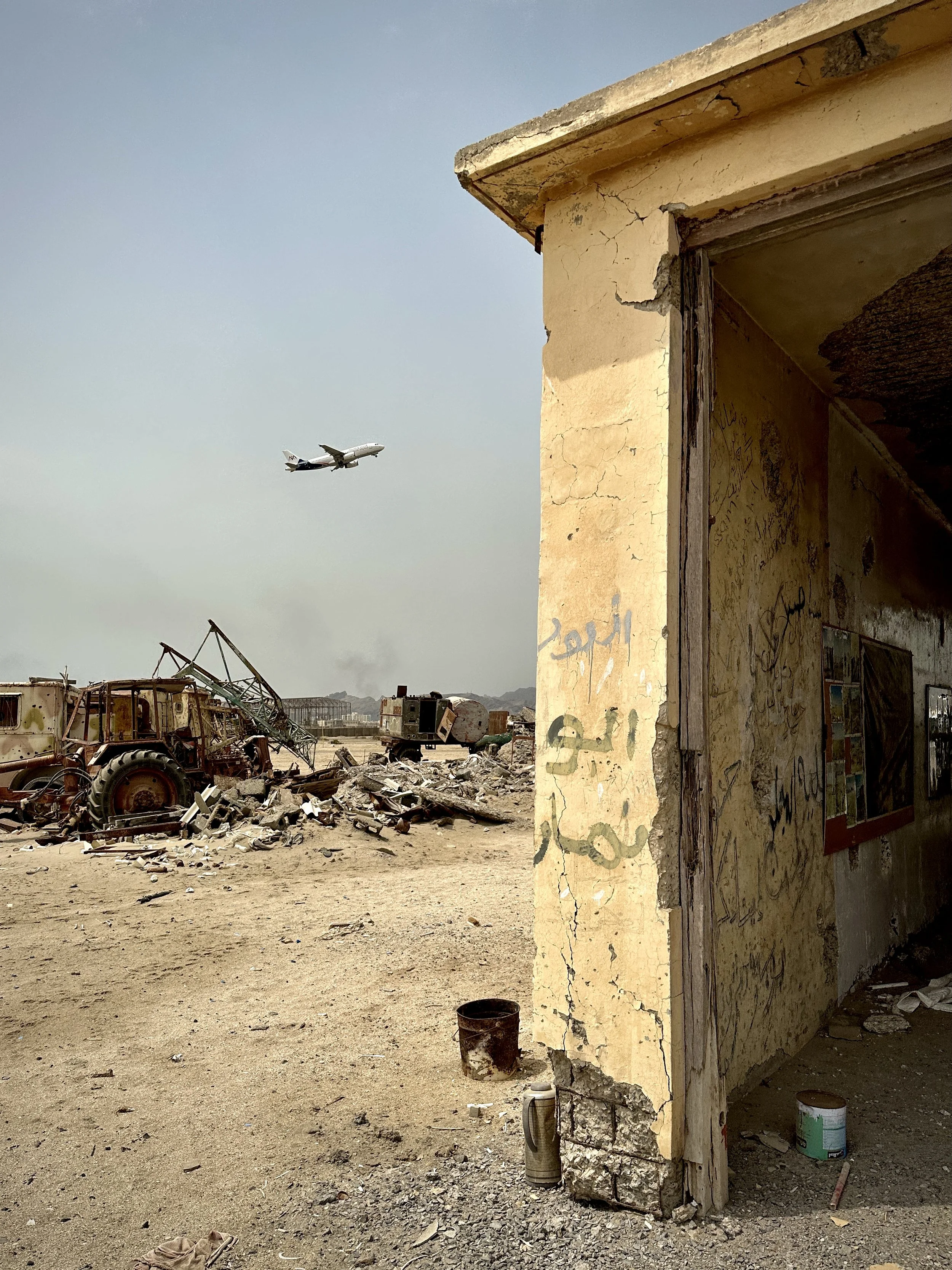 A commercial aircraft departs Aden International Airport beyond ruined structures left by war. While flights operate today, Project Masam teams continue removing mines and unexploded ordnance so passengers, workers and future airport expansion can be