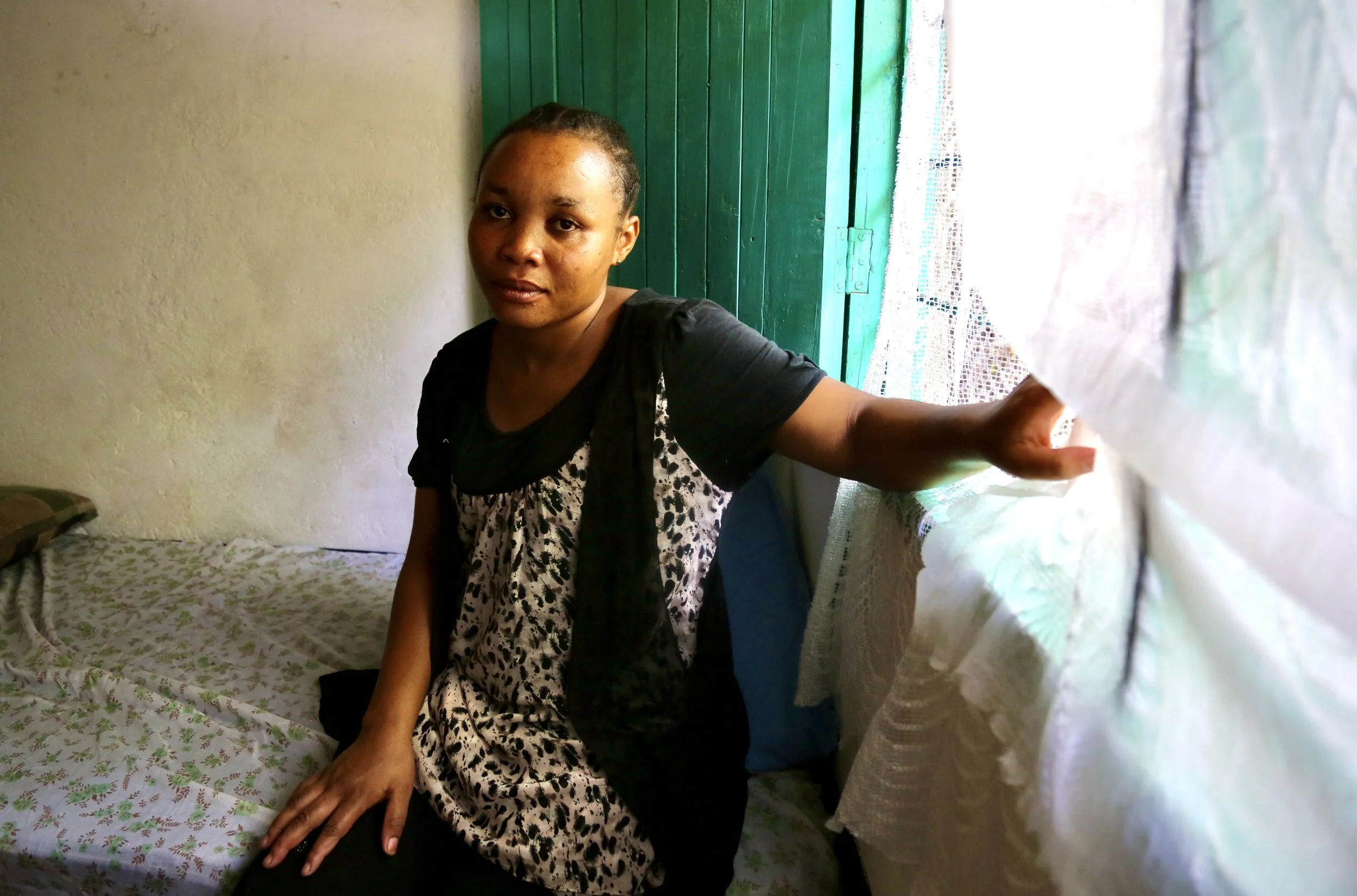 Clarisse, a Congolese refugee survivor of sexual violence, sits beside a curtained window in her room at the Safe Haven, where she began rebuilding her life through training and work.
