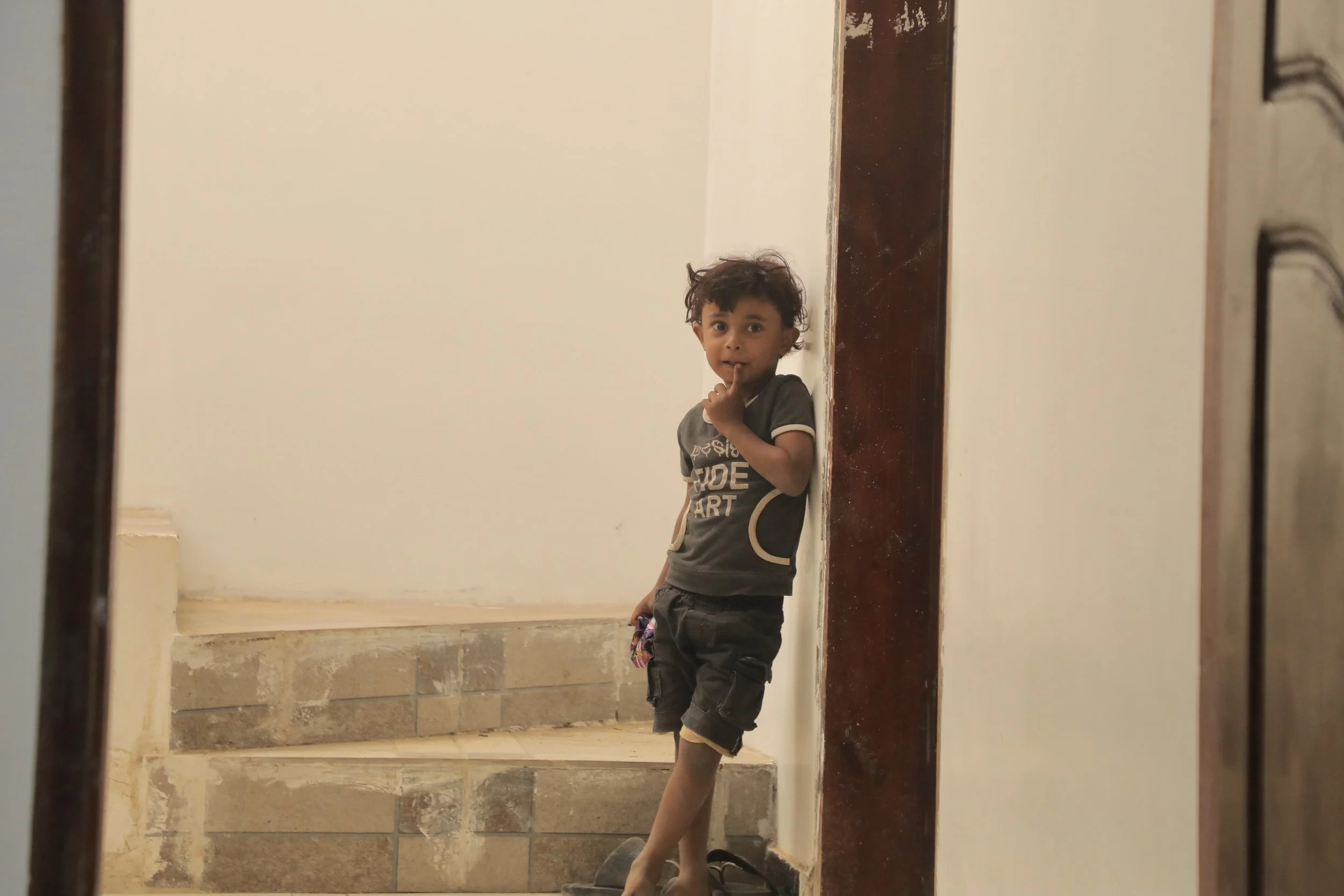 Sami’s young nephew lingers quietly in the doorway while the men inside discuss the war nearby. The adults repeatedly sent him away to play, trying to shield the children from conversations shaped by conflict and frontline life.