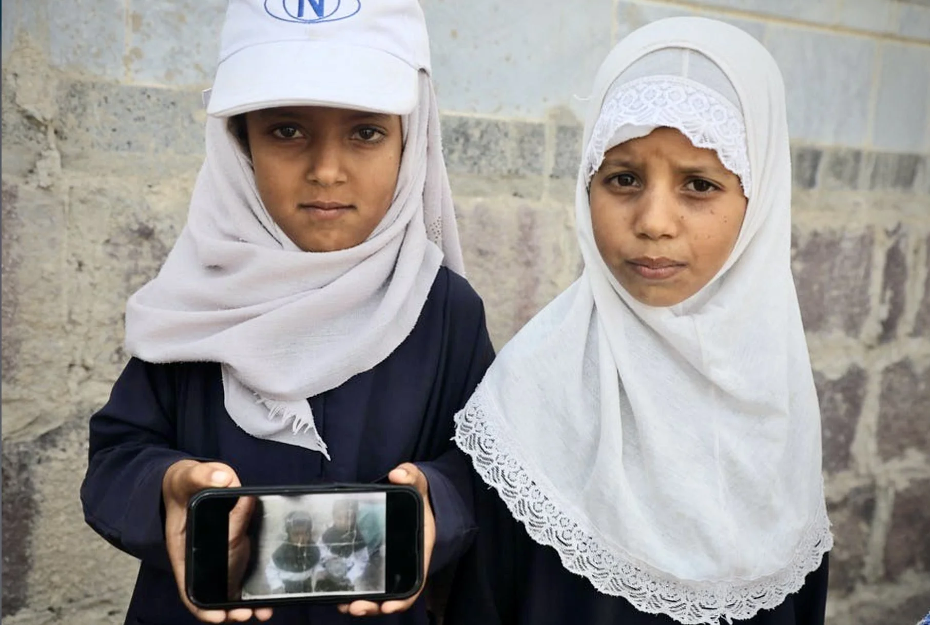Ilham, 7, and Iman, 5, daughters of Radwan Mohammed, hold up their father's evidence photograph of the anti-personnel landmines they discovered while playing marbles outside their home, Al Jadanah village, Shakhab, Al Dhale. 