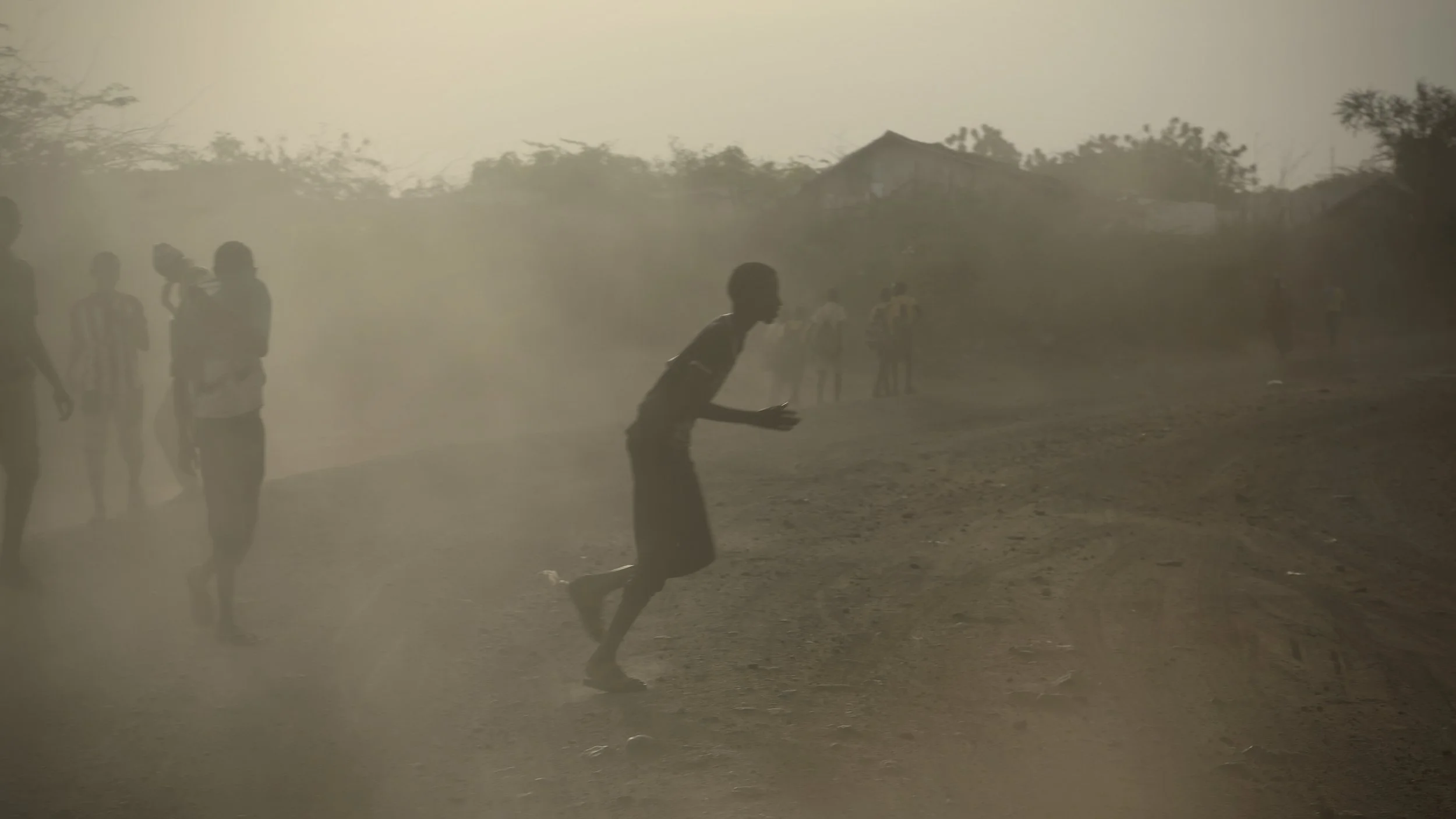 A South Sudanese teen runs through evening dust on a road inside Kakuma.
