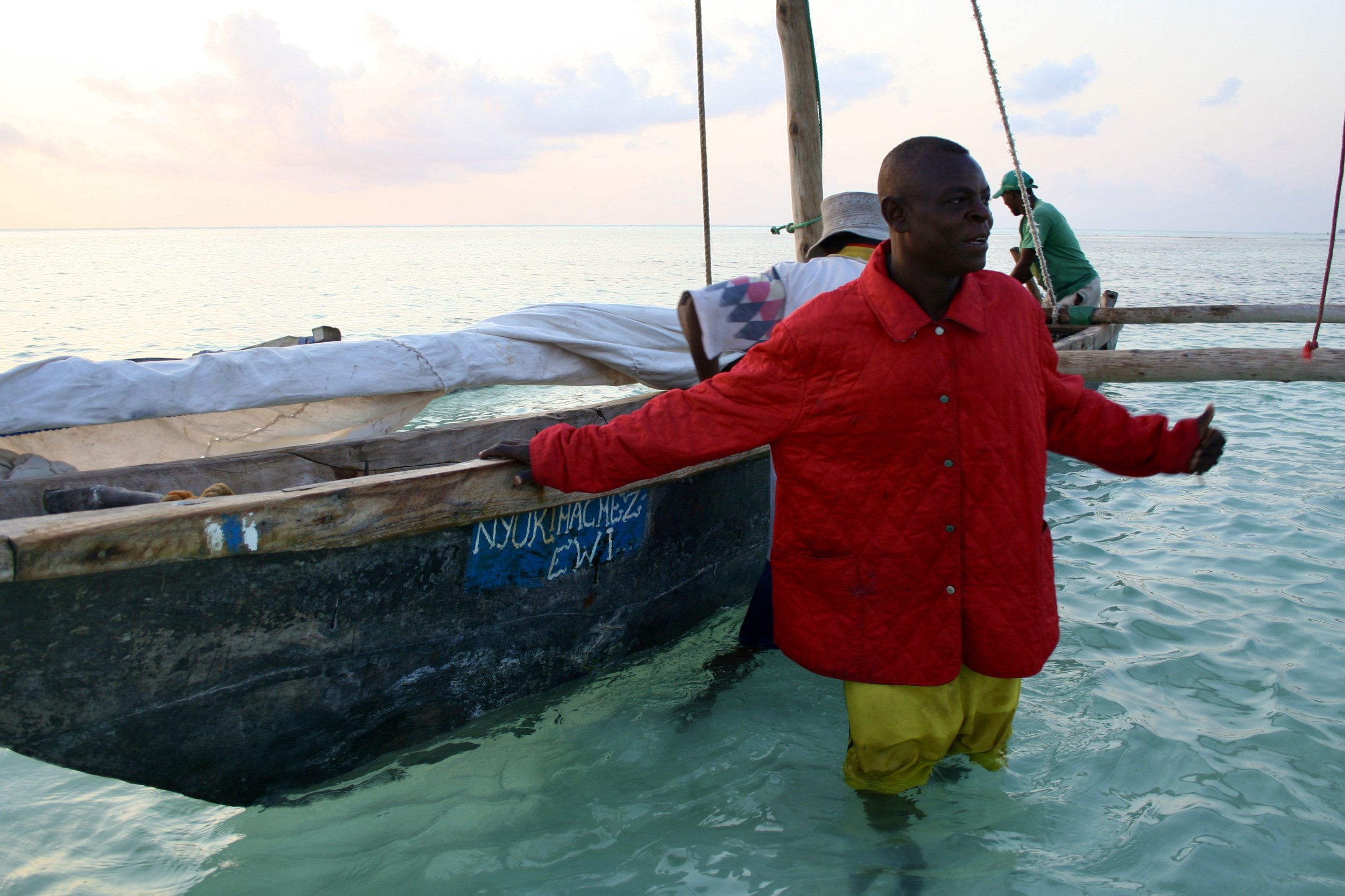 Captain Fruit wades out through the shallows to Nyuki Machezi, the hand-painted name of the family dhow visible on its hull.