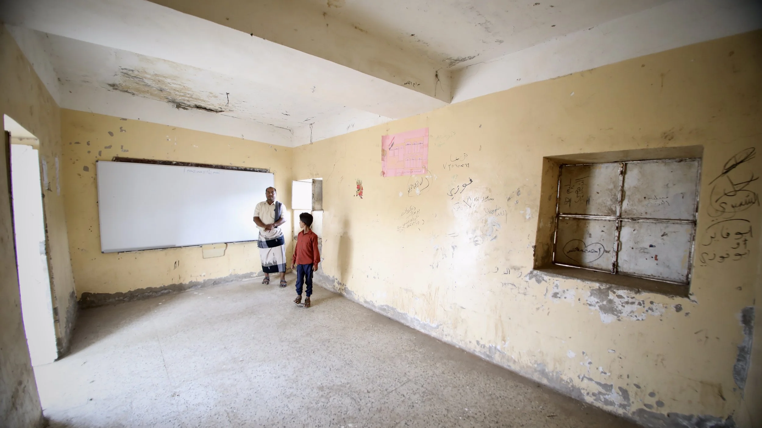 School Director  Ahmad Mohamad Al Barakani, 33, and his son Marwan, stand inside an empty classroom at Al Shaab School, where some rooms remain unusable due to conflict damage.