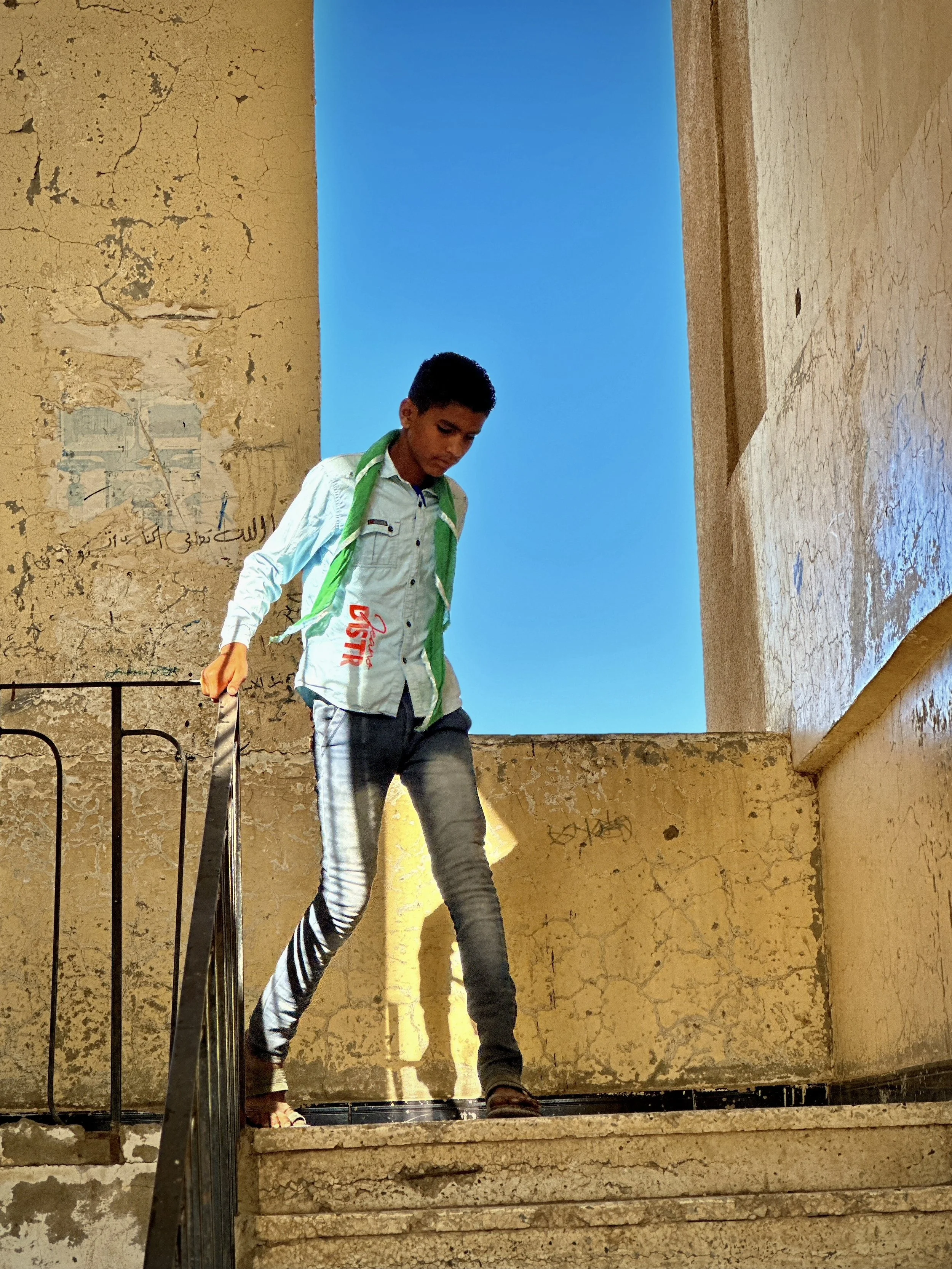 A student wearing a green prefect’s scarf walks through a damaged stairwell at Ibrahim Aqeel School in Taiz. Parts of the school were destroyed after landmines and improvised explosive devices stored there during the war exploded, leaving students to