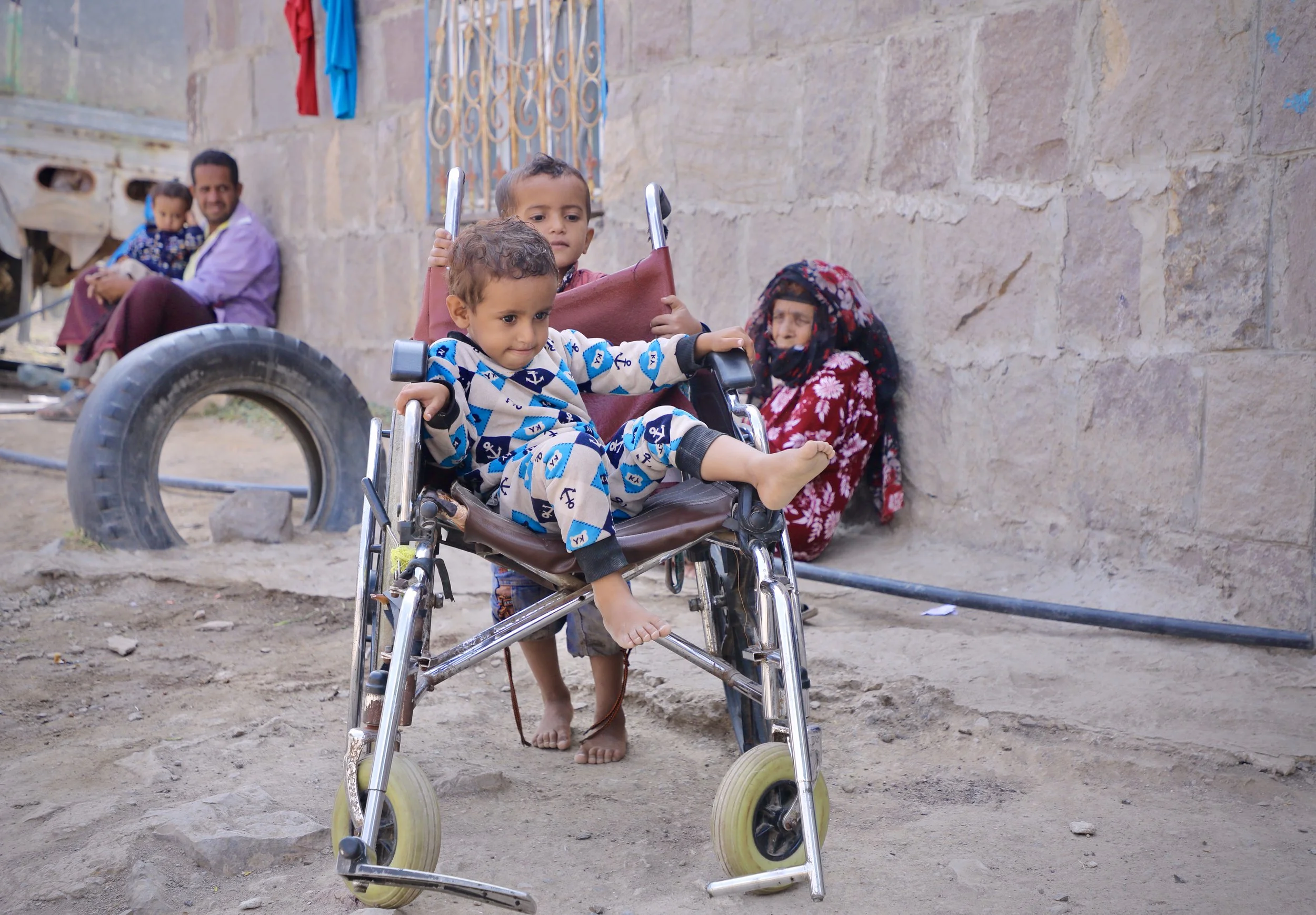 A grandchild plays in Mosaid Mohammed Ali Naji's wheelchair in the courtyard of his home, Shakhab, Al Dhale. The wheelchair - used by Mosaid when outside the compound - has become a toy. The great-grandmother of the family is seated against the wall 