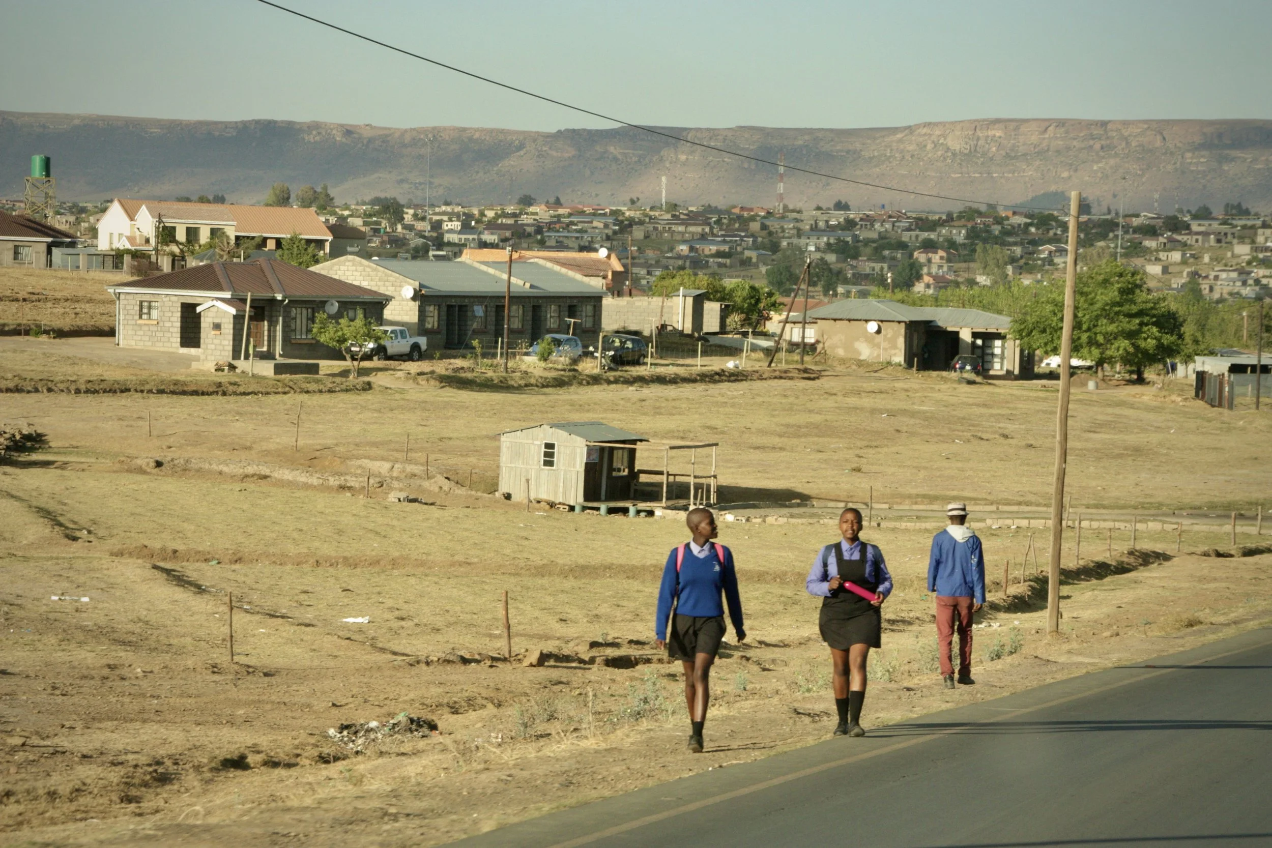 Children walk along the roadside outside Ha Chonapase in Leribe District, Lesotho. Michael’s grandchildren walk long distances to attend school because the family cannot afford daily transport costs. Secondary education in Lesotho often requires fami
