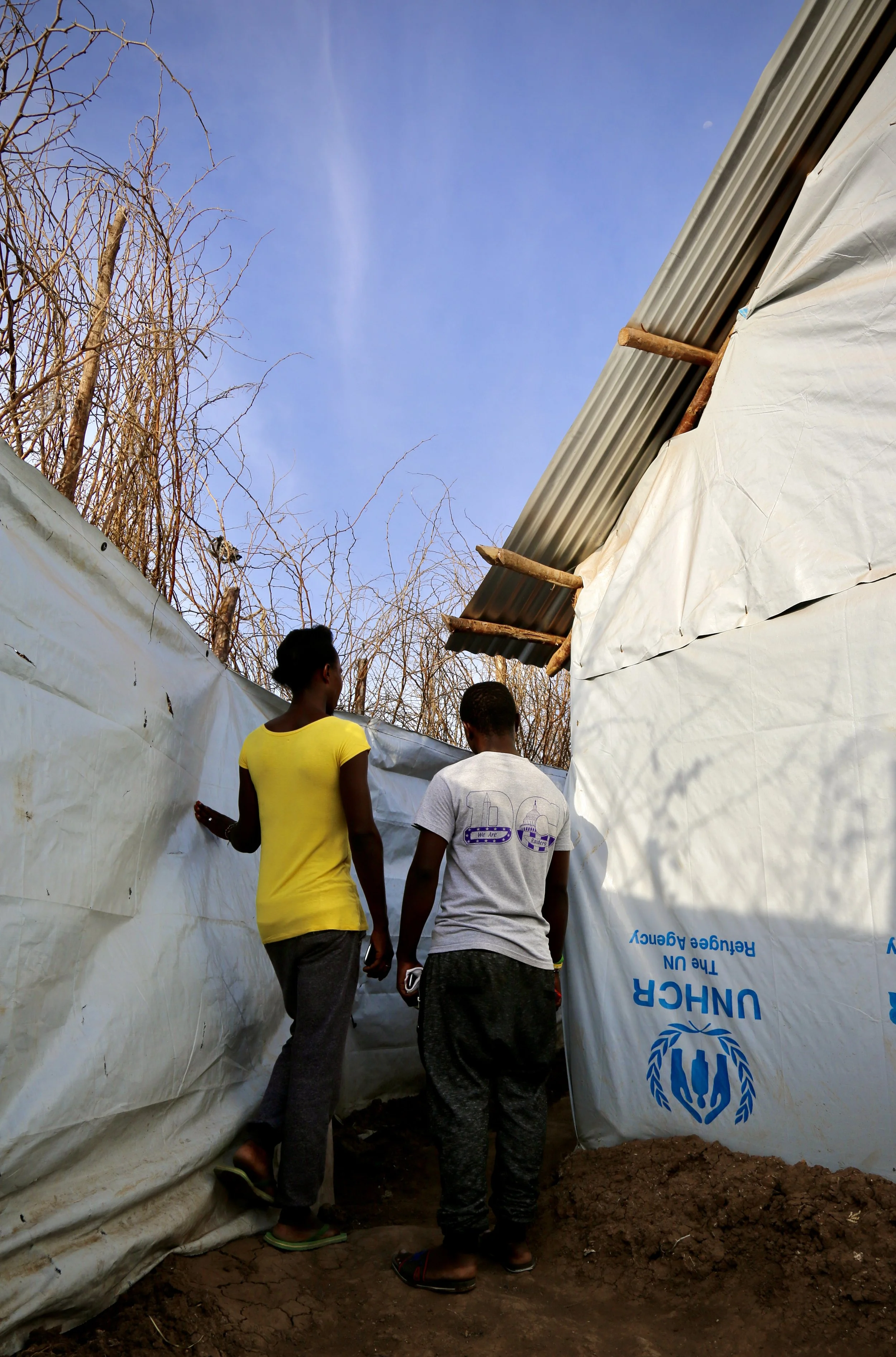 Residents walk through narrow passageways between shelters built from UNHCR tarpaulin, corrugated metal and thorn branches inside Kakuma refugee camp.