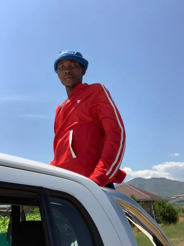Peer educator P., a former herd boy, rides on the back of the outreach vehicle as the team travels through the lowlands of Leribe district, Lesotho, to reach the meeting point for an HIV and sexually transmitted infection (STI) prevention session wit