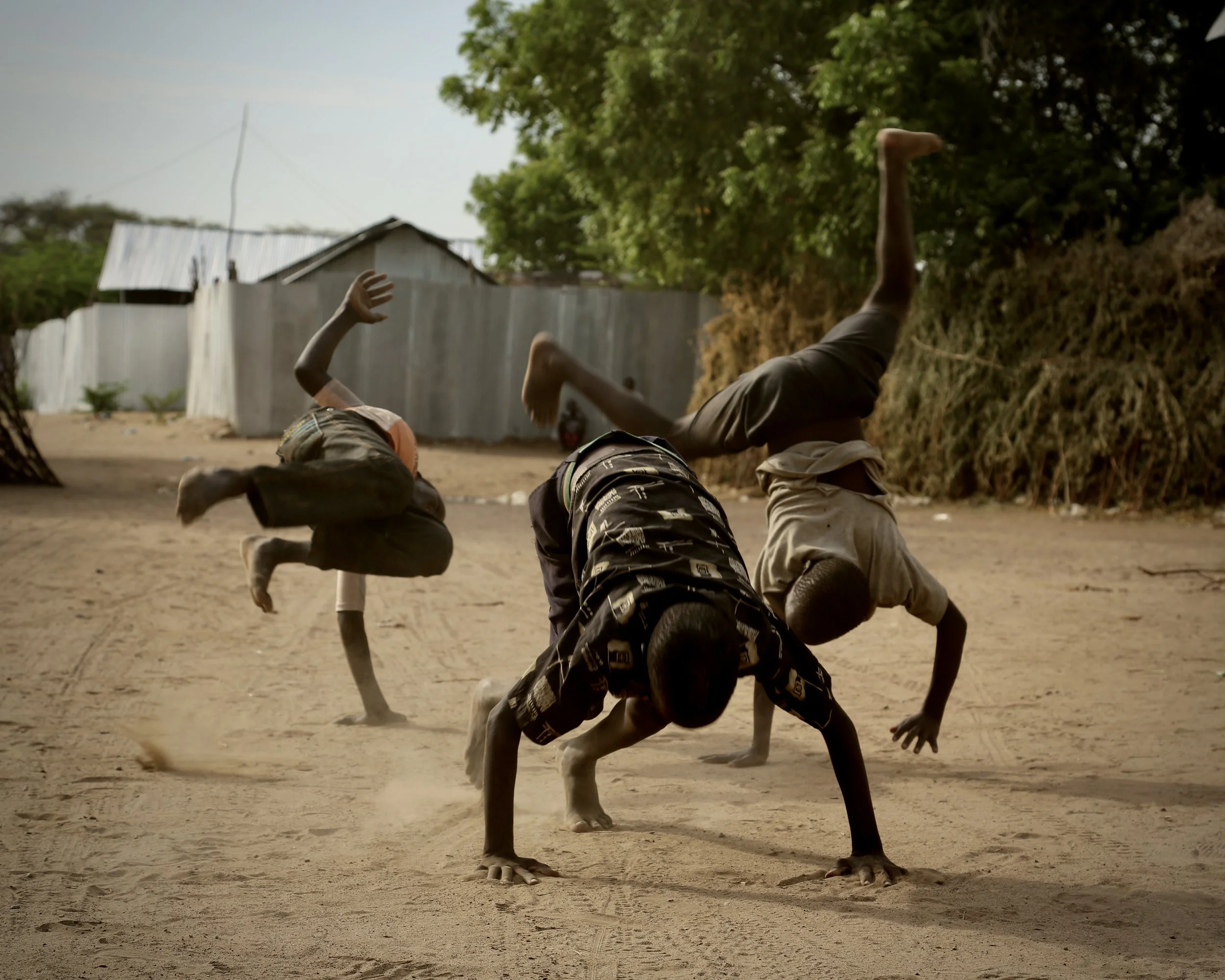 Boys perform handstands and flips in an open space in Kakuma refugee camp.