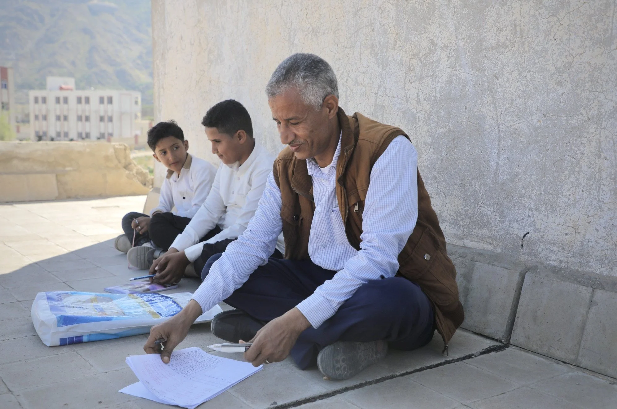Abdulghani al-Haidari, director of Ibrahim Aqeel School, sits on the rooftop beside students during exam sessions at the school in Taiz, Yemen. After classrooms and administrative buildings were damaged following the discovery of landmines and improv