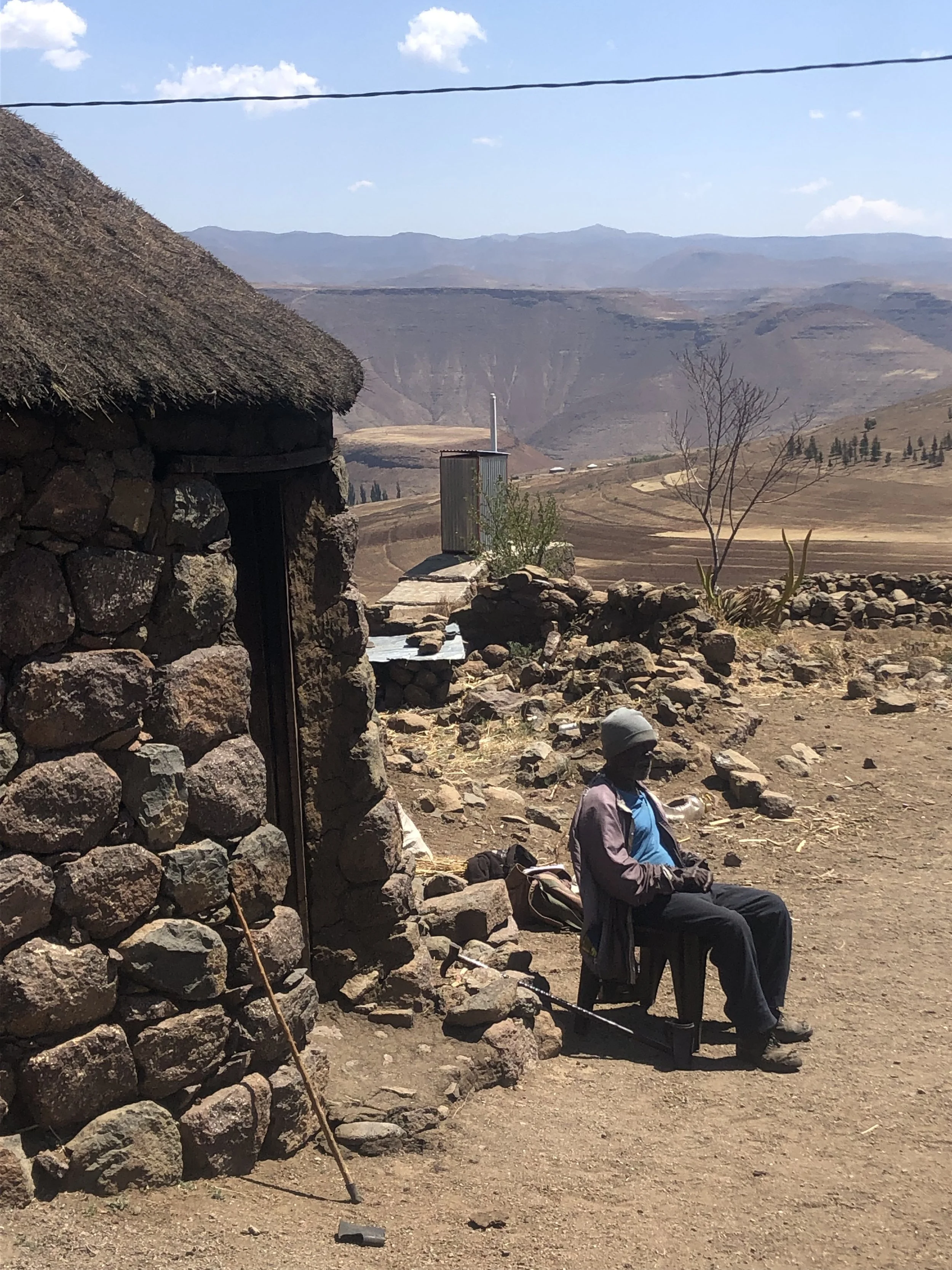 An elderly man sits outside the stone hut he shared with teenager Bokang Khera in Thaba Moorosi. Bokang helped herd cattle, while the older man provided food, shelter and daily care. The two lived alone together in the mountains.