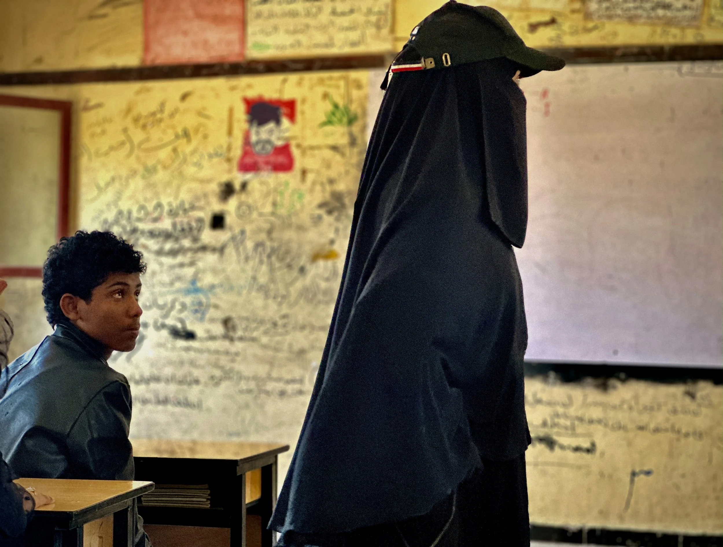 A teacher stands inside a classroom at Ibrahim Aqeel School in Taiz, Yemen, as a student looks up during lessons. 