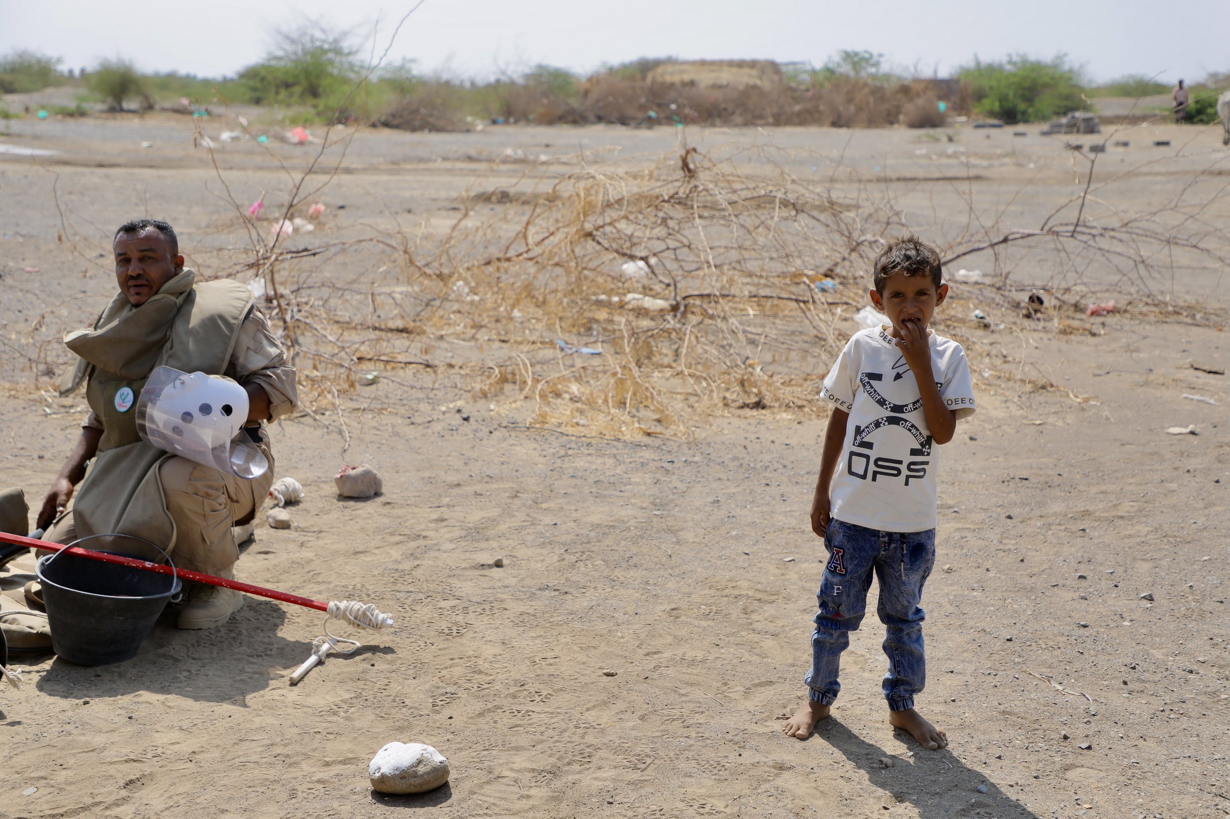 A child stands near a deminer at a marked site in Al Remah, near Mocha, Taiz governorate, Yemen. Children frequently encounter demining activity as part of their everyday environment.