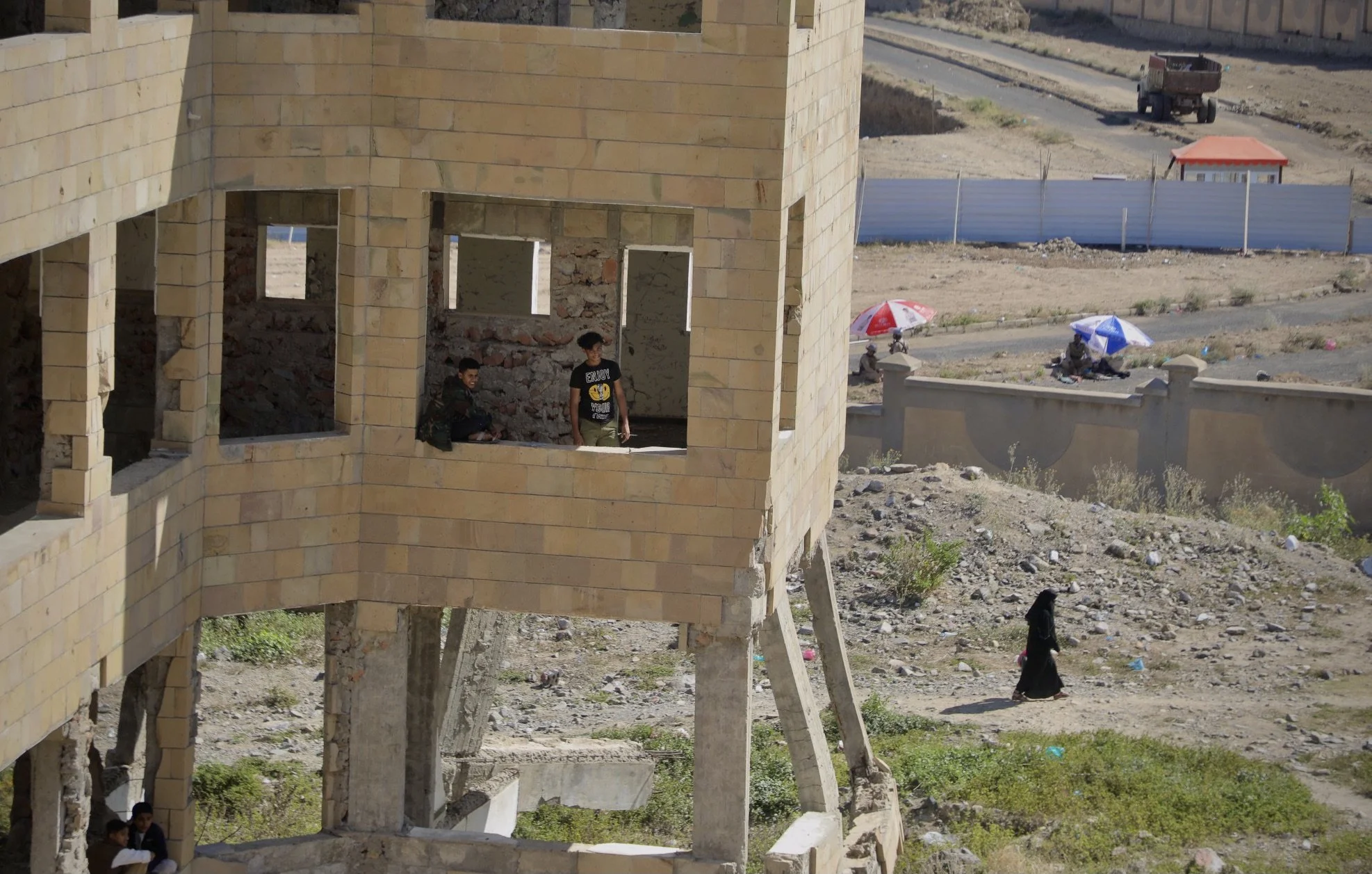 Students gather inside a heavily damaged section of Ibrahim Aqeel School in Taiz, Yemen, where buildings were left partially destroyed after landmines and improvised explosive devices stored at the school exploded during the conflict. In the backgrou