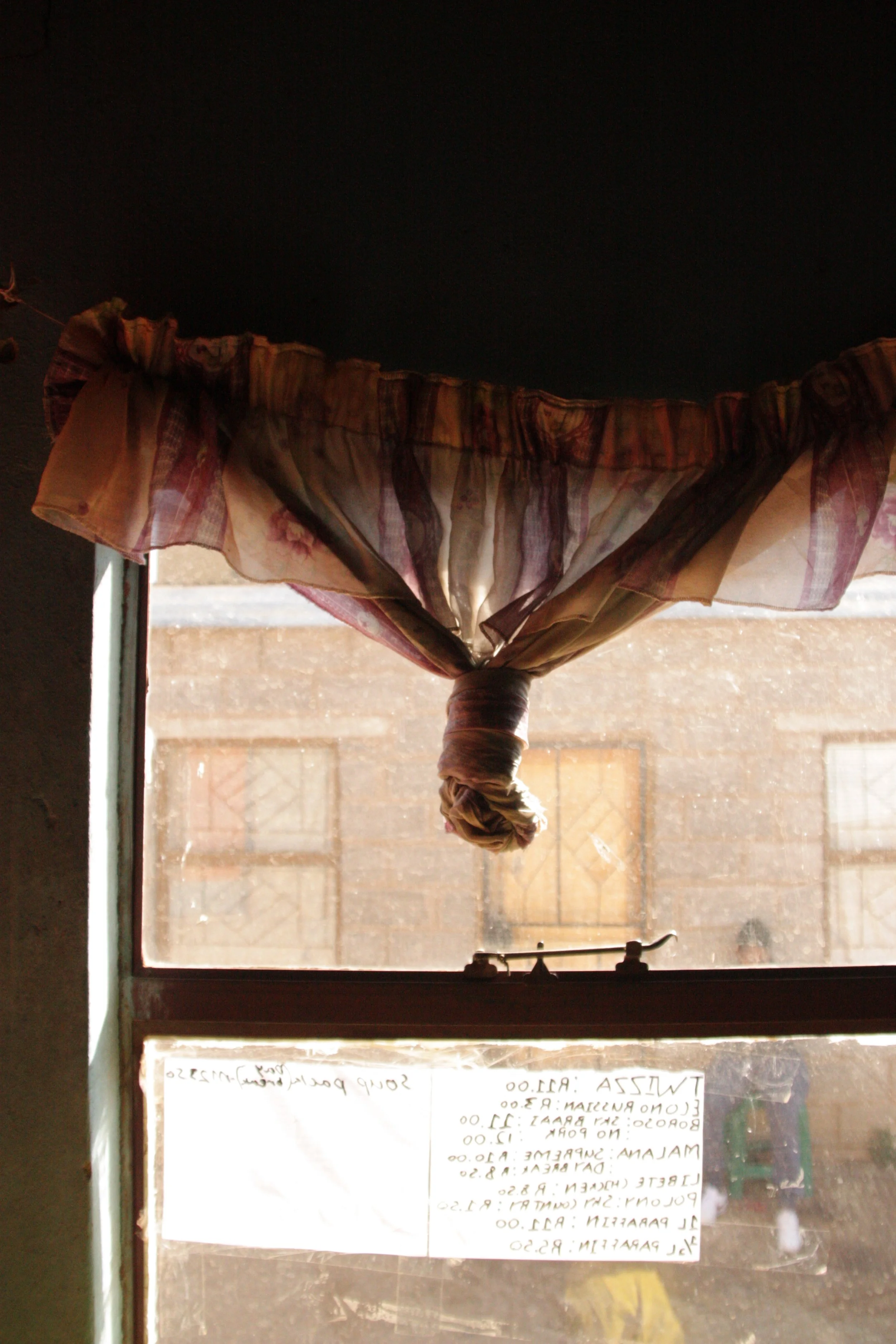 A curtain hangs over the window of Paballo’s small shop in Ha Magele, Leribe District, Lesotho, where handwritten prices for bread, paraffin and snacks are taped to the glass. With youth unemployment high and economic opportunities limited, many wome