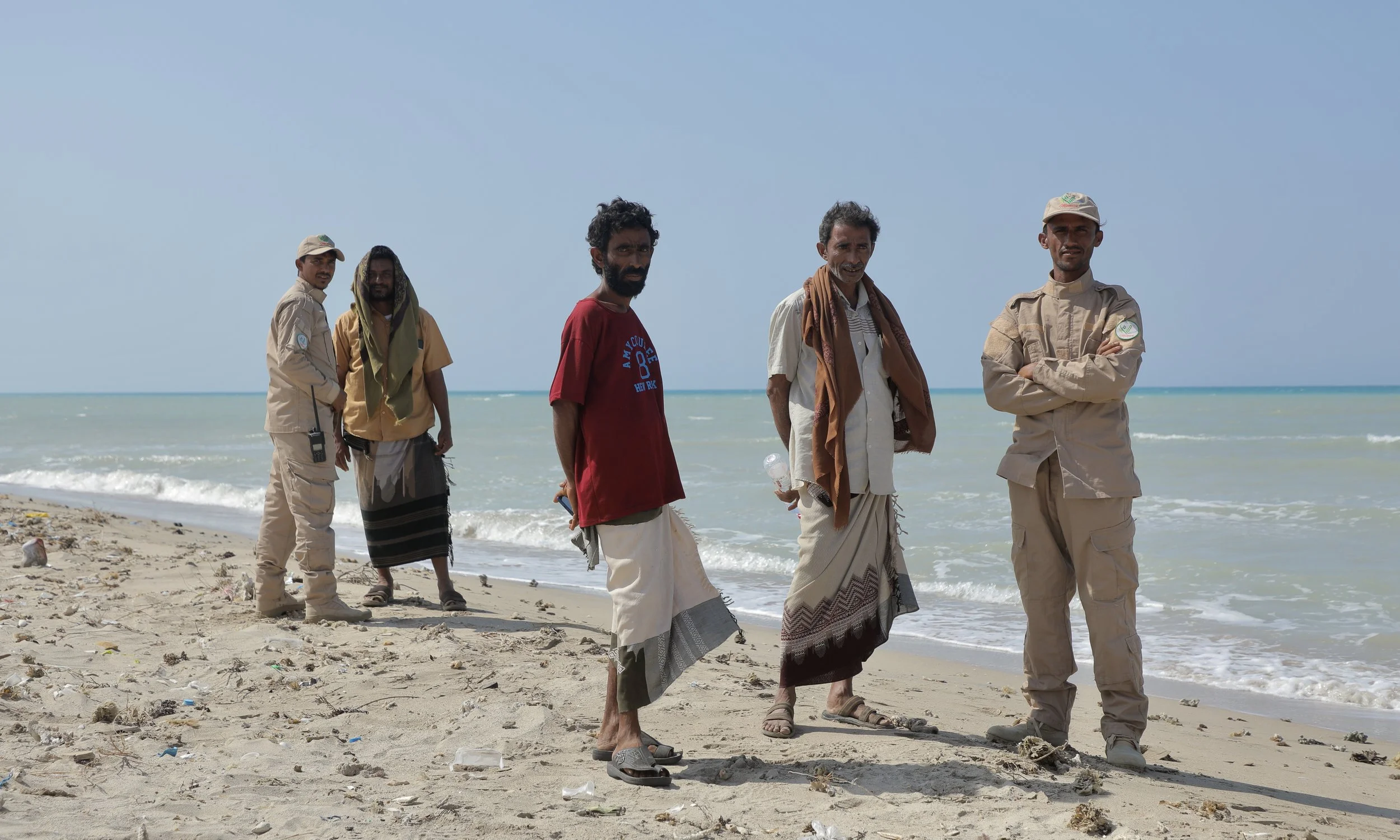 Members of the local community and a security guard stand along the shoreline near a mine clearance site north of Al Khokha.