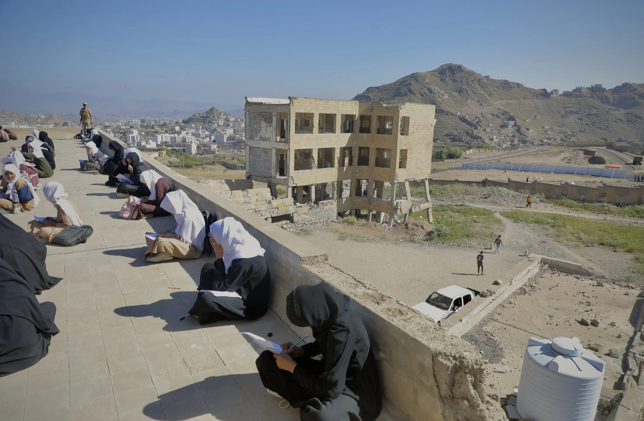 Students sit on the rooftop of Ibrahim Aqeel School overlooking damaged sections of the campus in Taiz, where classrooms were destroyed in an explosion linked to landmines and improvised explosive devices stored at the site during the war.