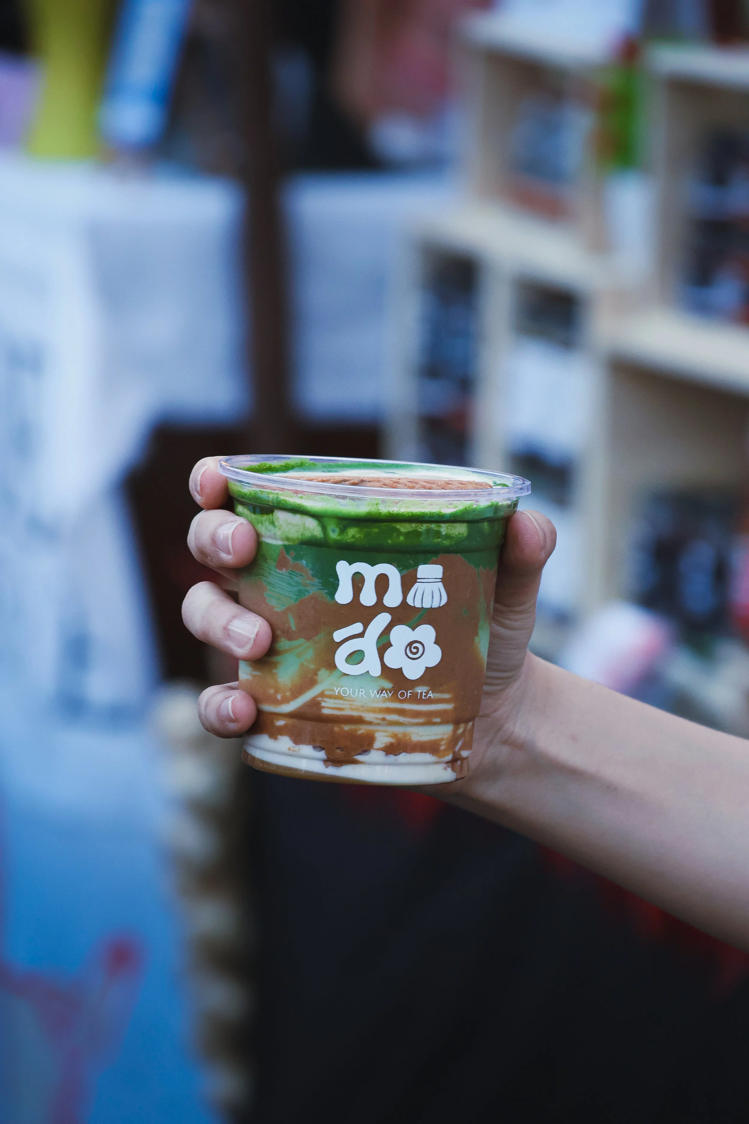 A hand holding a cup of tea or beverage in a store aisle.