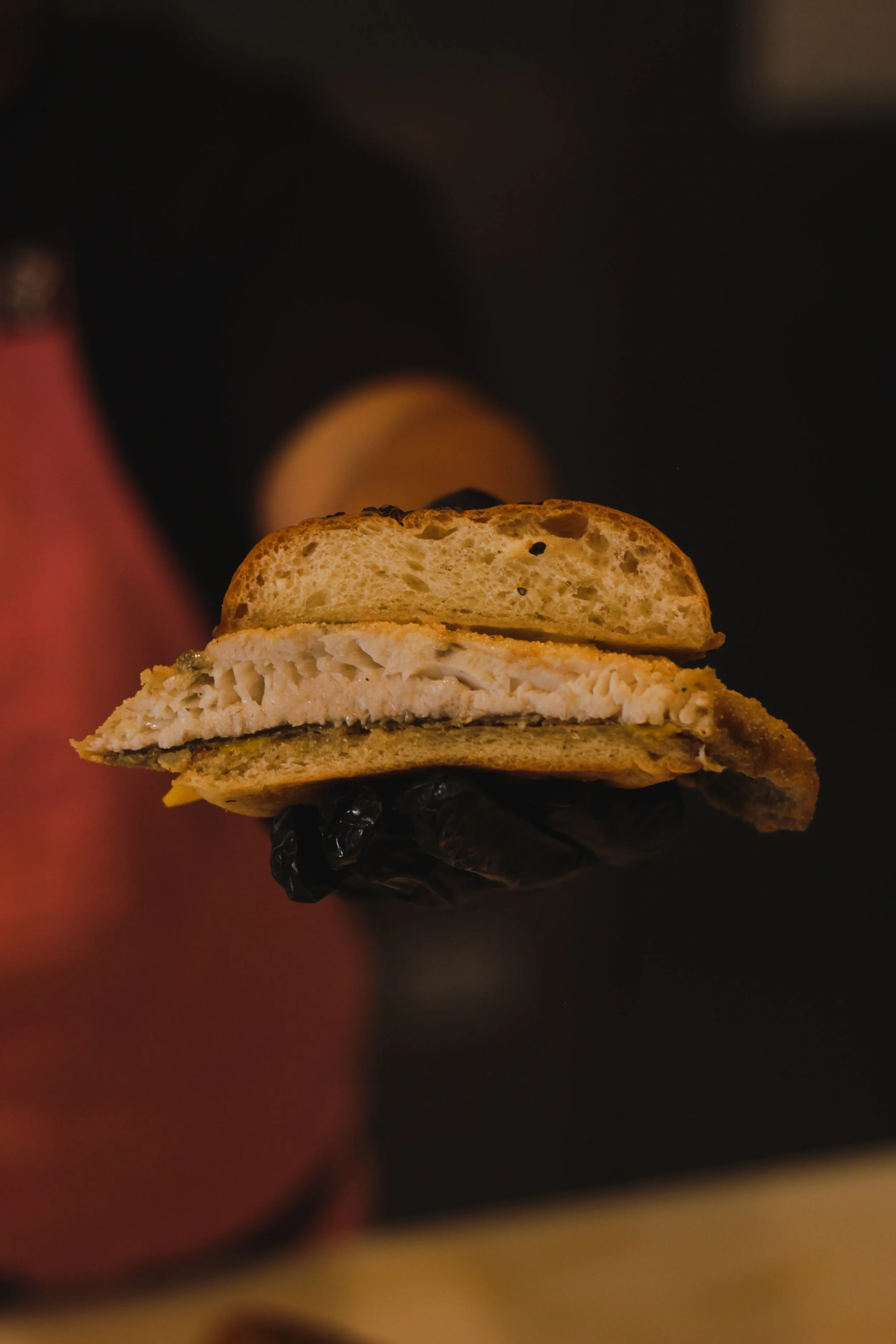 Close-up of a sliced piece of fish cake with black beans and seasonings, held by a hand in a black glove.