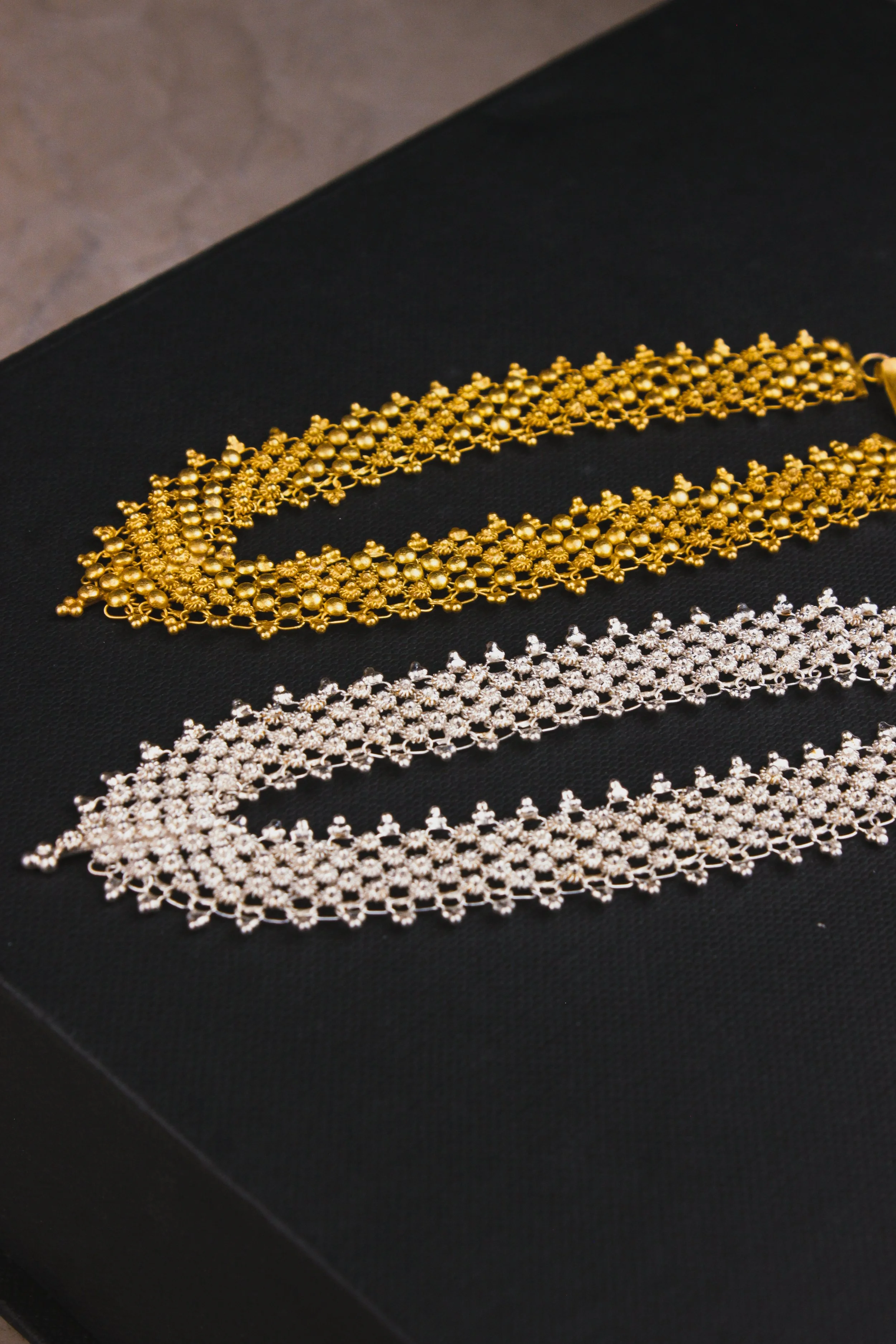 Close-up of gold and silver jeweled necklaces on a black surface.
