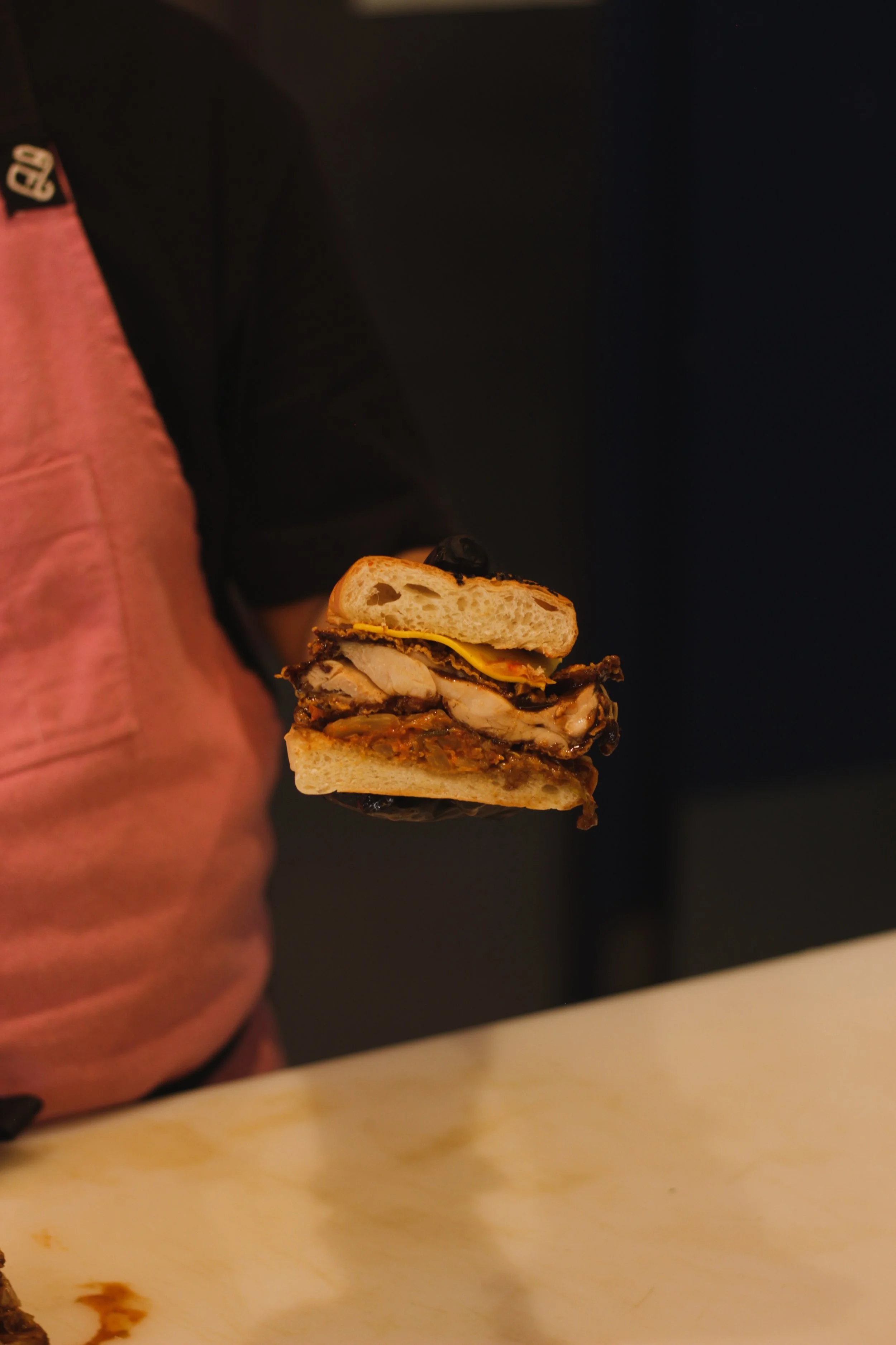 A person holding a sandwich with sliced chicken, cheese, and vegetables inside a bun.