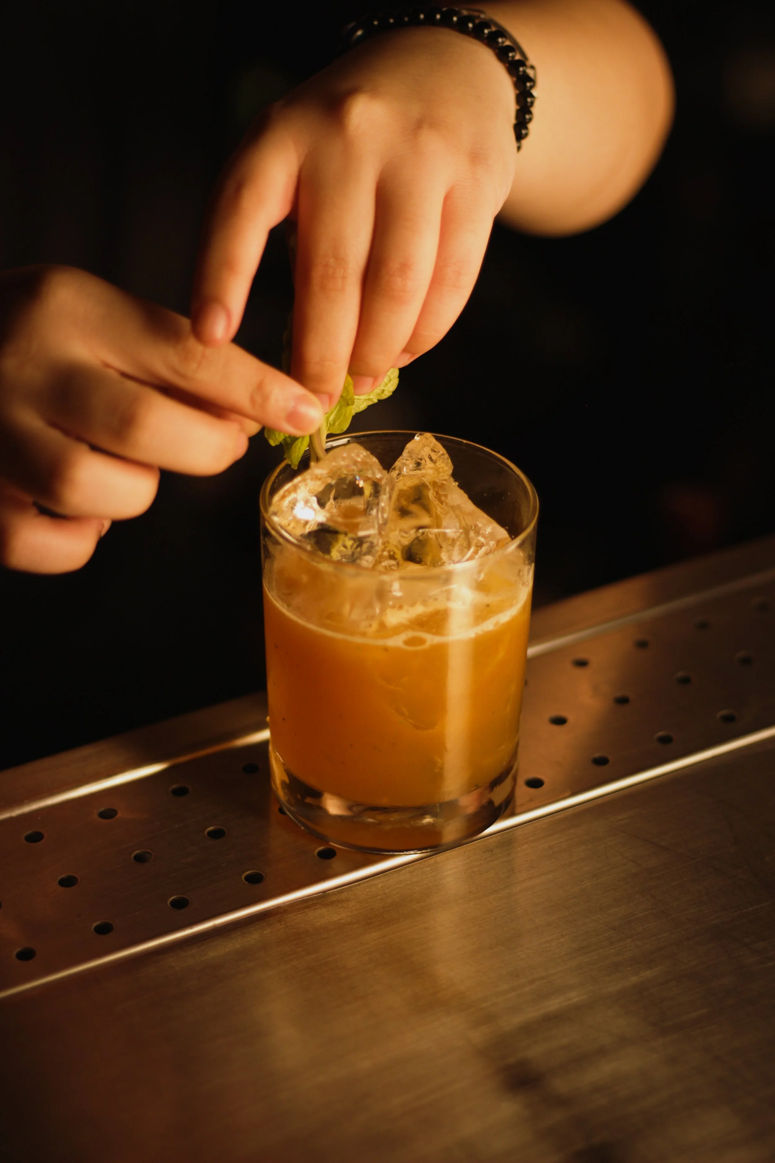 A person's hand garnishing a cocktail with a sprig of mint.