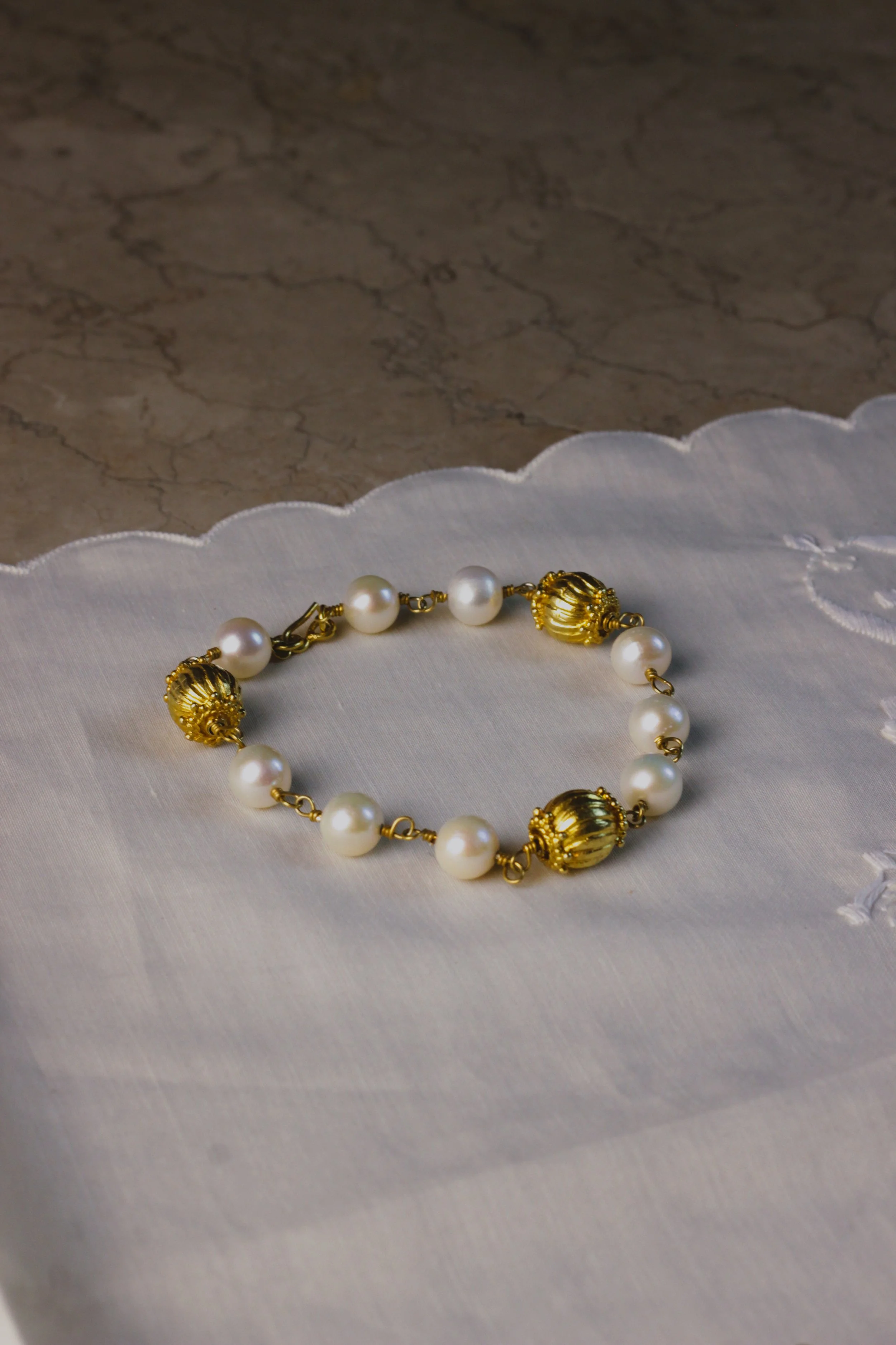 A pearl and gold necklace on white fabric with scalloped edges, placed on a marble surface.