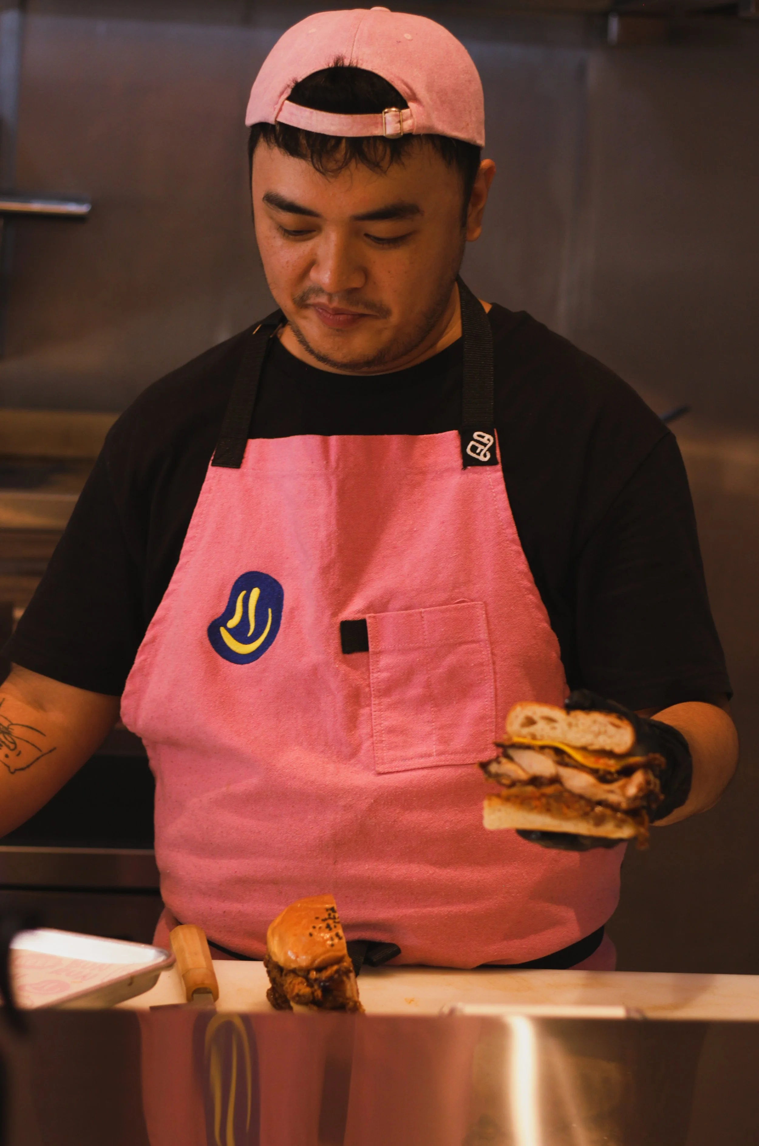 A person wearing a pink cap and pink apron preparing sandwiches in a kitchen.