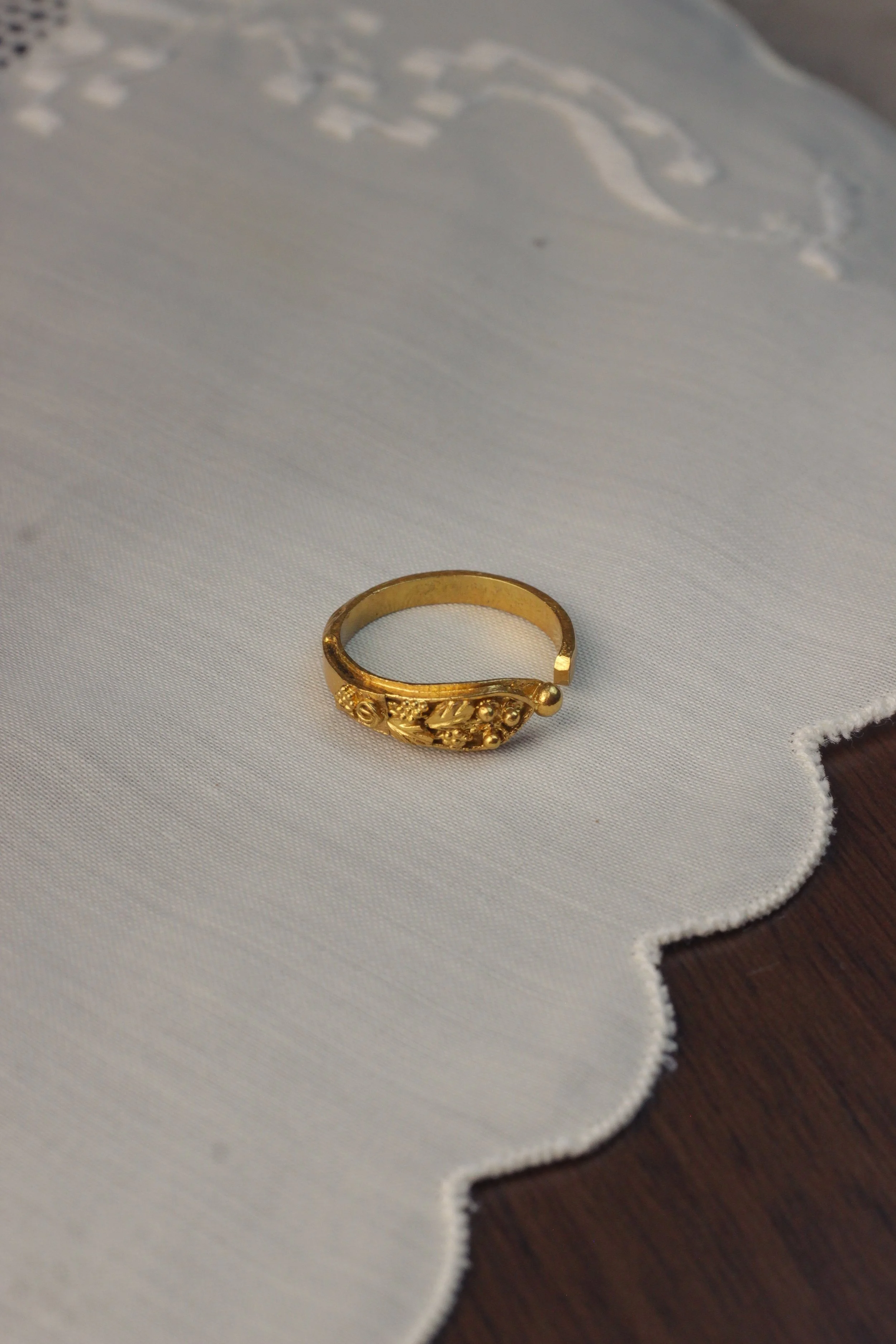 A gold ring with intricate designs placed on white fabric with scalloped edges.