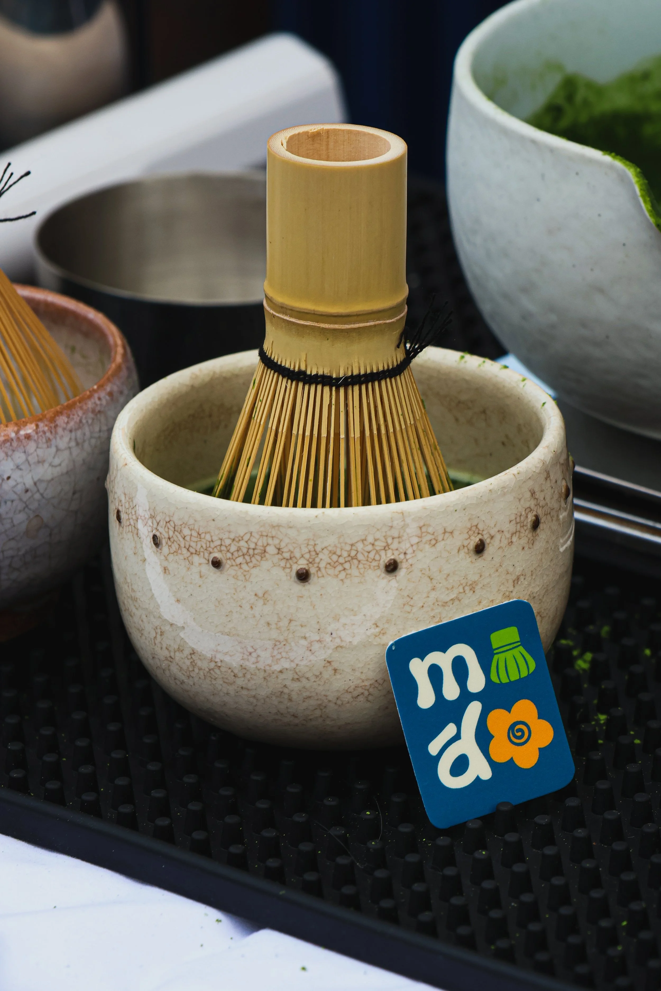 Ceramic bowls and a bamboo sushi mat displayed on a black surface, with partial view of a blue sticker that has white text and an orange flower design.