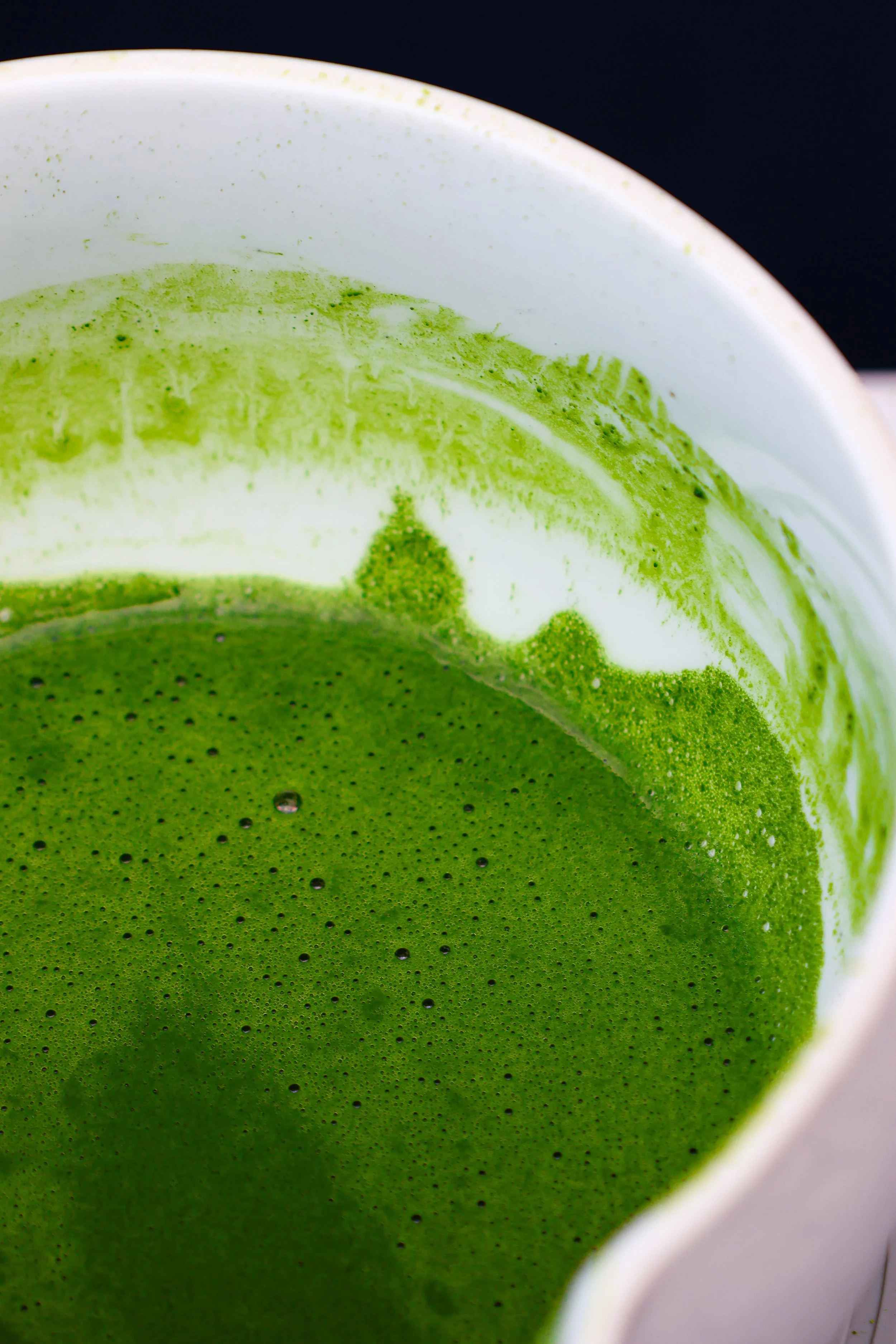 Close-up of a white cup with green matcha tea, showing the vibrant green surface and some bubbles.