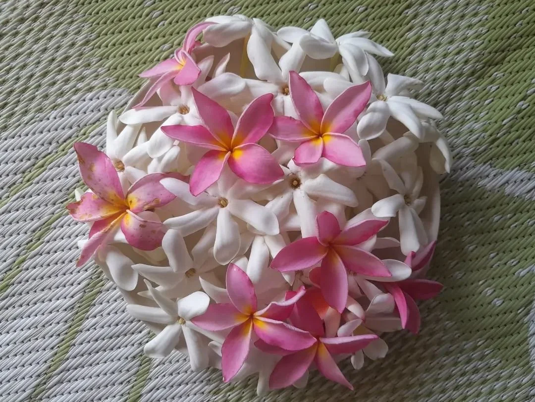 A bouquet of pink and white frangipani flowers on a woven green and beige mat.